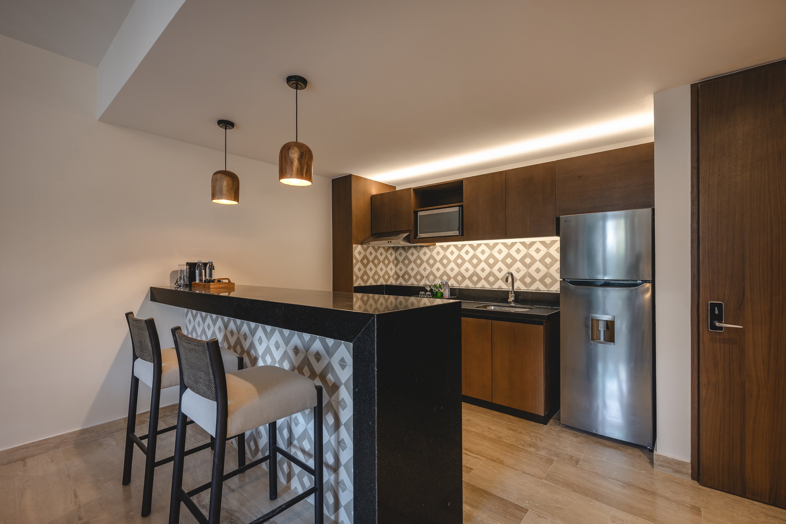 Cocina moderna con isla y sillas, gabinetes de madera, refrigerador de acero inoxidable, microondas, día con iluminación suave.