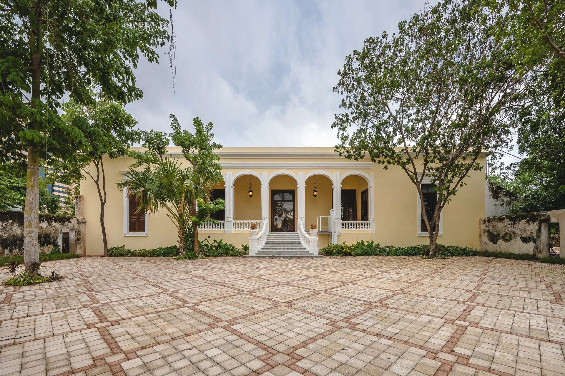 Casa de estilo clásico con entrada principal de escalones y columnas, rodeada de árboles y un patio de ladrillos.