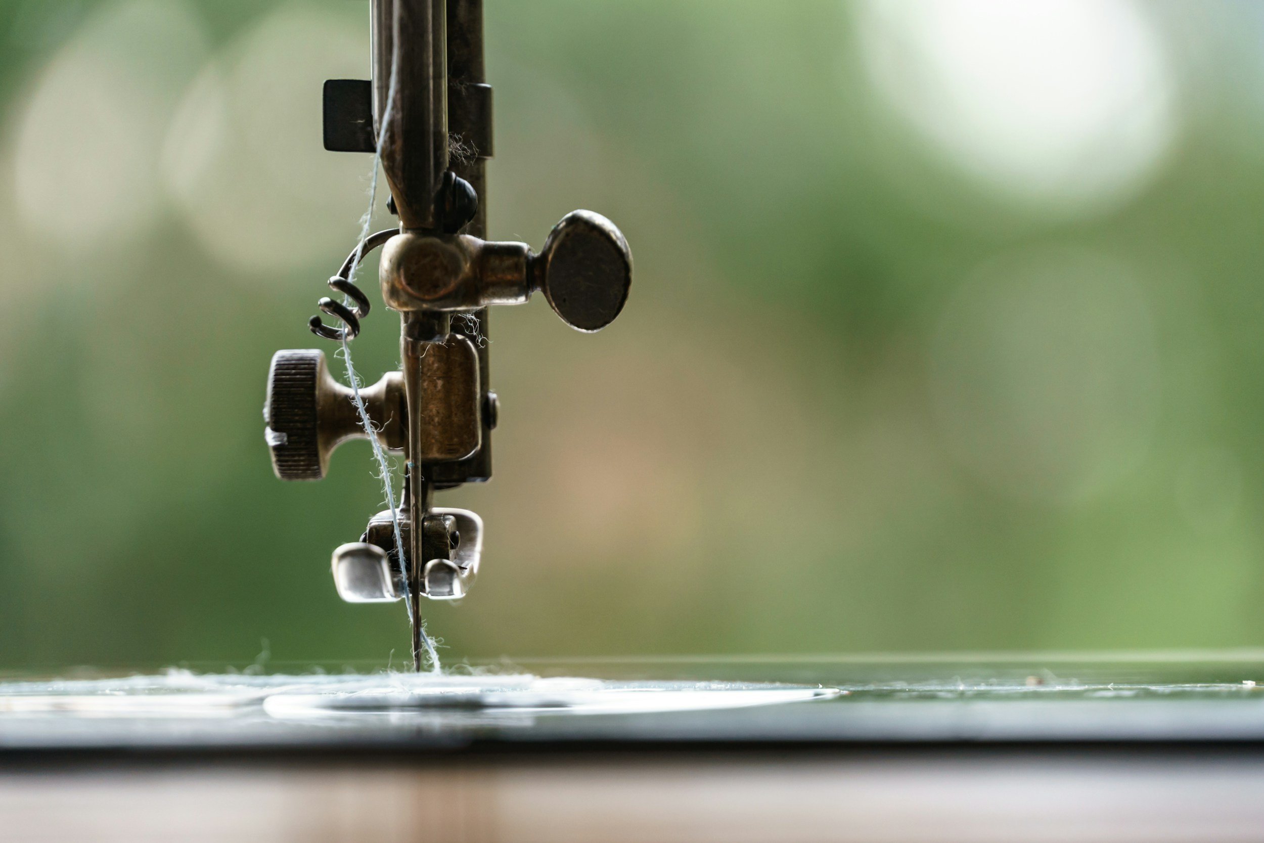 Close-up of an embroidery machine needle and presser foot, with fabric underneath, in a sewing workshop.