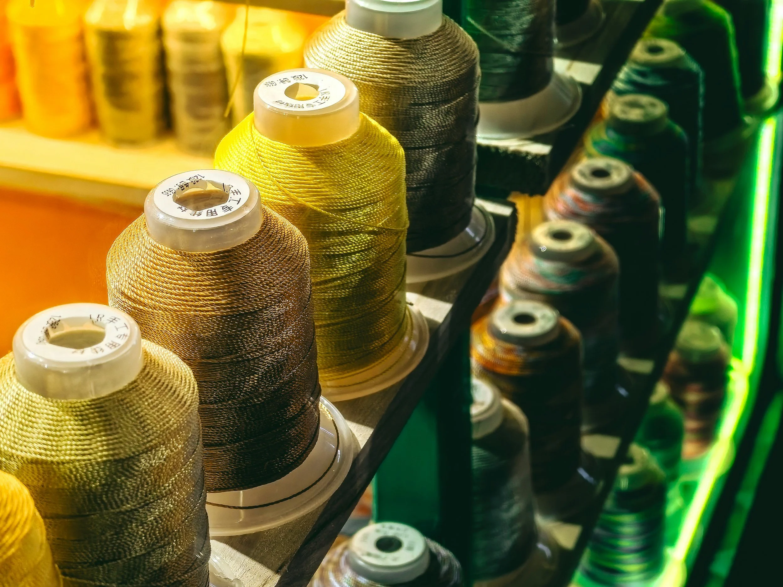 Close-up of  colorful spools of thread in yellow, black, and multicolored hues, arranged on a display rack in a sewing or craft store.