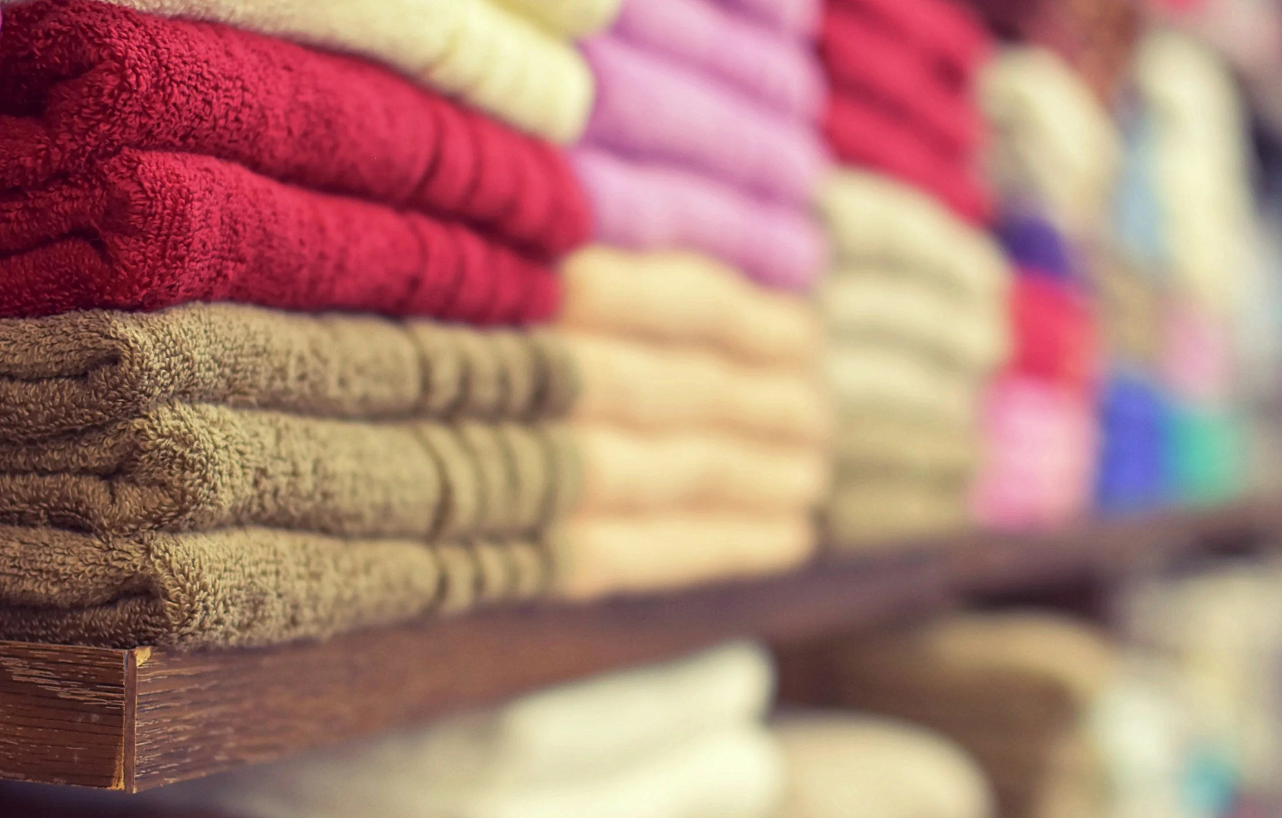 Stacked colorful towels arranged on a wooden shelf.