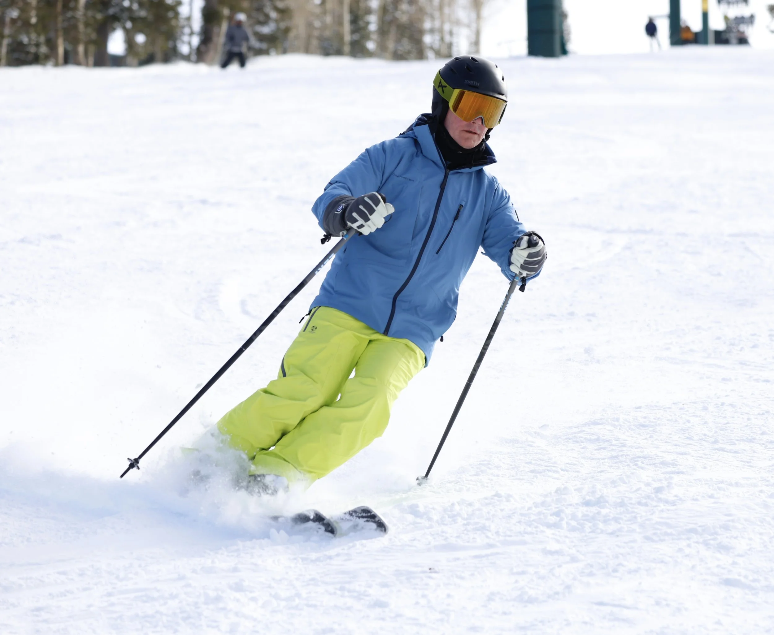 A person dressed in bright yellow ski pants, a blue ski jacket, and a black helmet skiing on a snowy slope.
