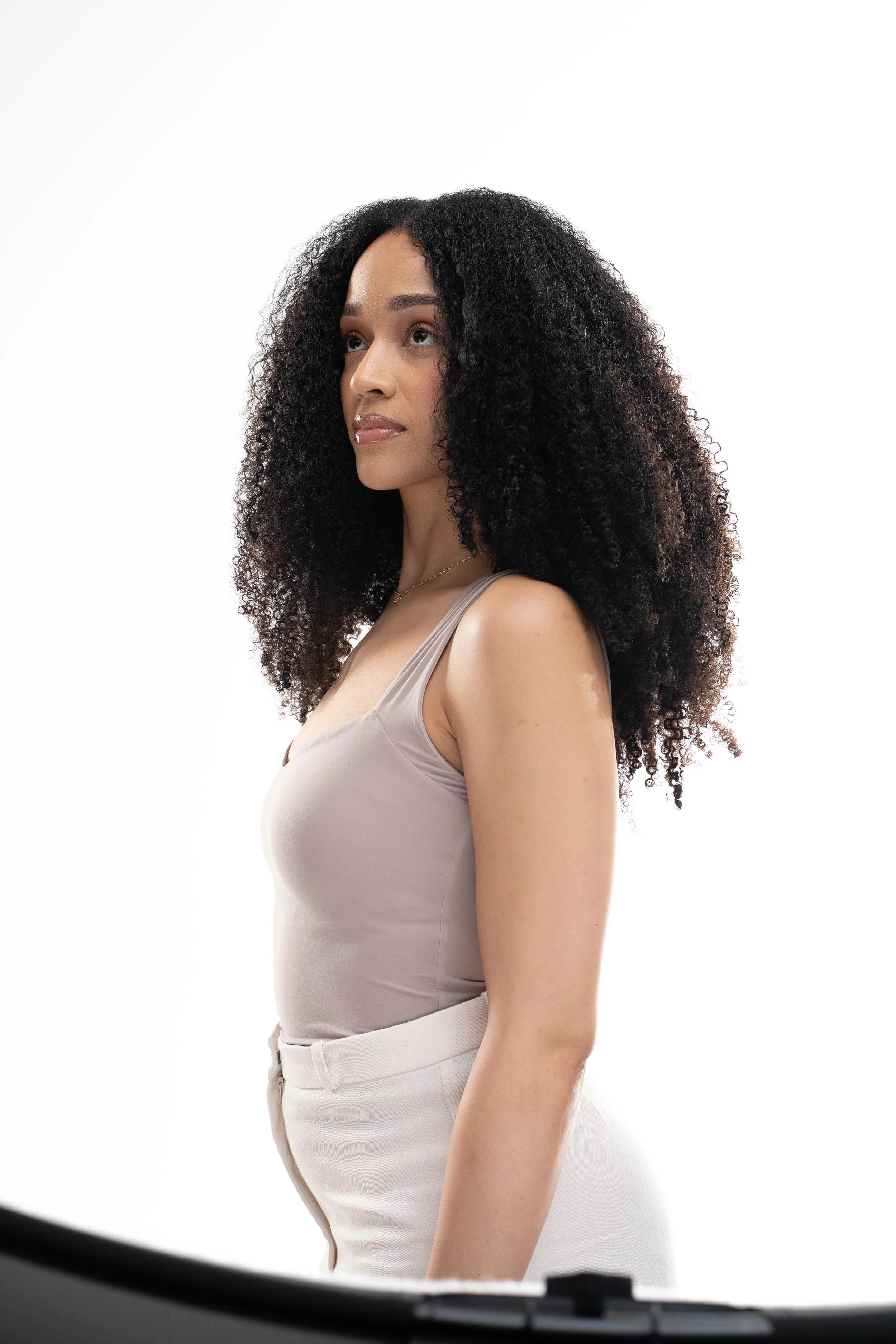 Black woman wearing Love Luxury curly raw afro curly hair bundles in a beige top, natural hair and sew-in client Kansas City