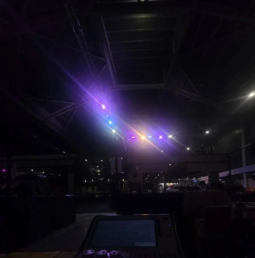 Indoor parking garage illuminated with colorful stage lights, with vehicles visible and equipment in the foreground.