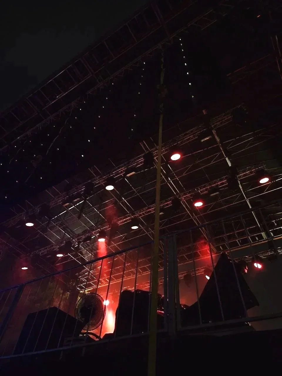 Stage with overhead rigging and red lighting, with smoke or fog effects and stage equipment visible.