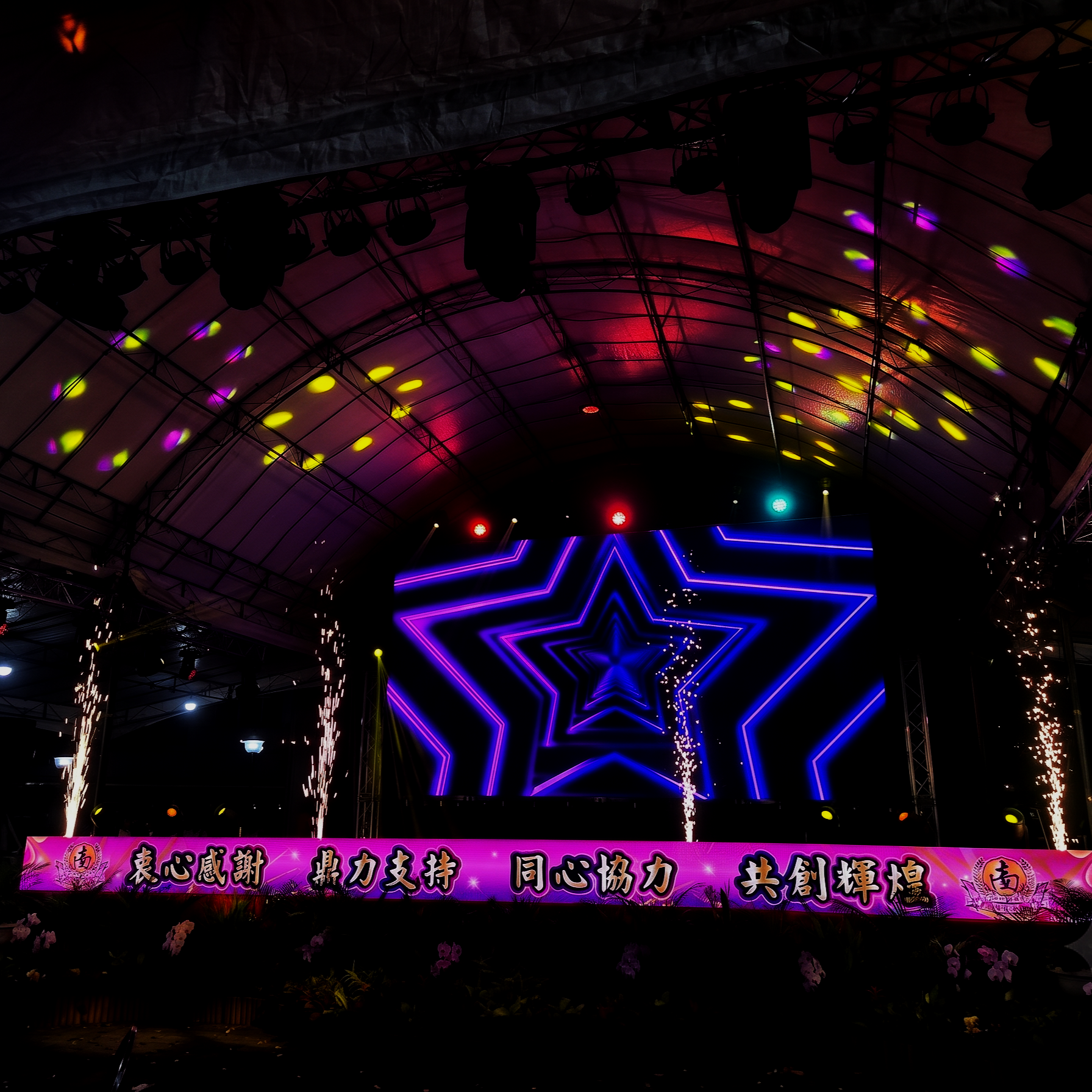 Stage with neon star design, colorful lights, fireworks, and a pink banner with Chinese characters.