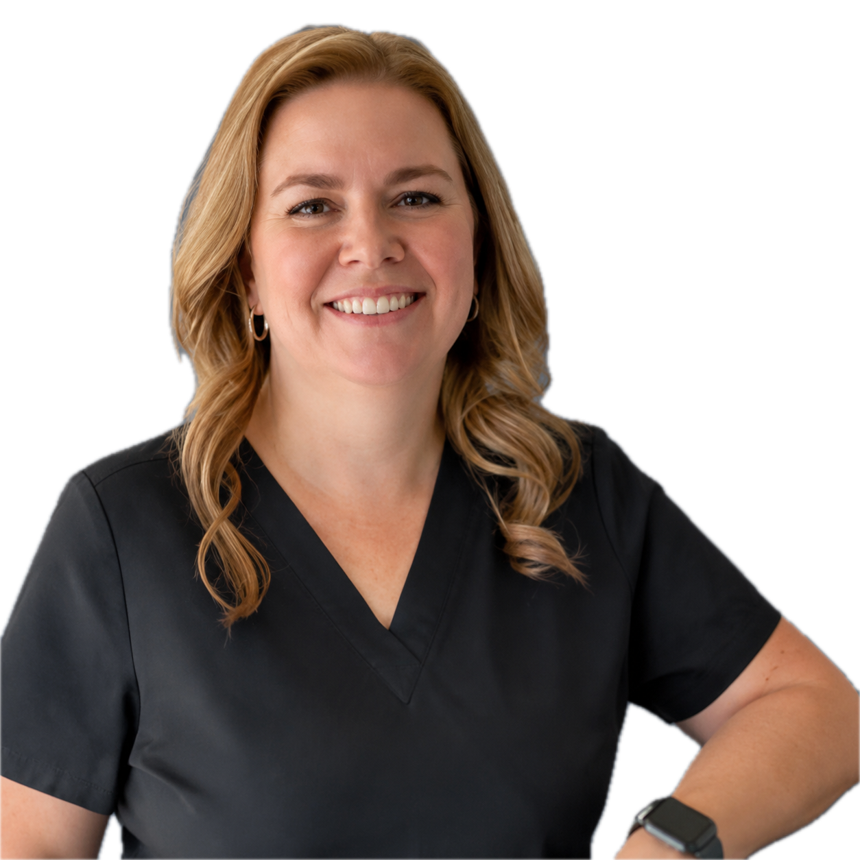 A woman with shoulder-length wavy blonde hair, smiling, wearing black medical scrubs and earrings, with her right arm resting on a surface and wearing a smartwatch on her left wrist.