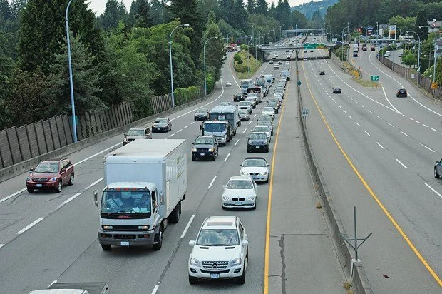 Traffic jam on a multi-lane highway with cars and trucks lined up, surrounded by greenery and trees.