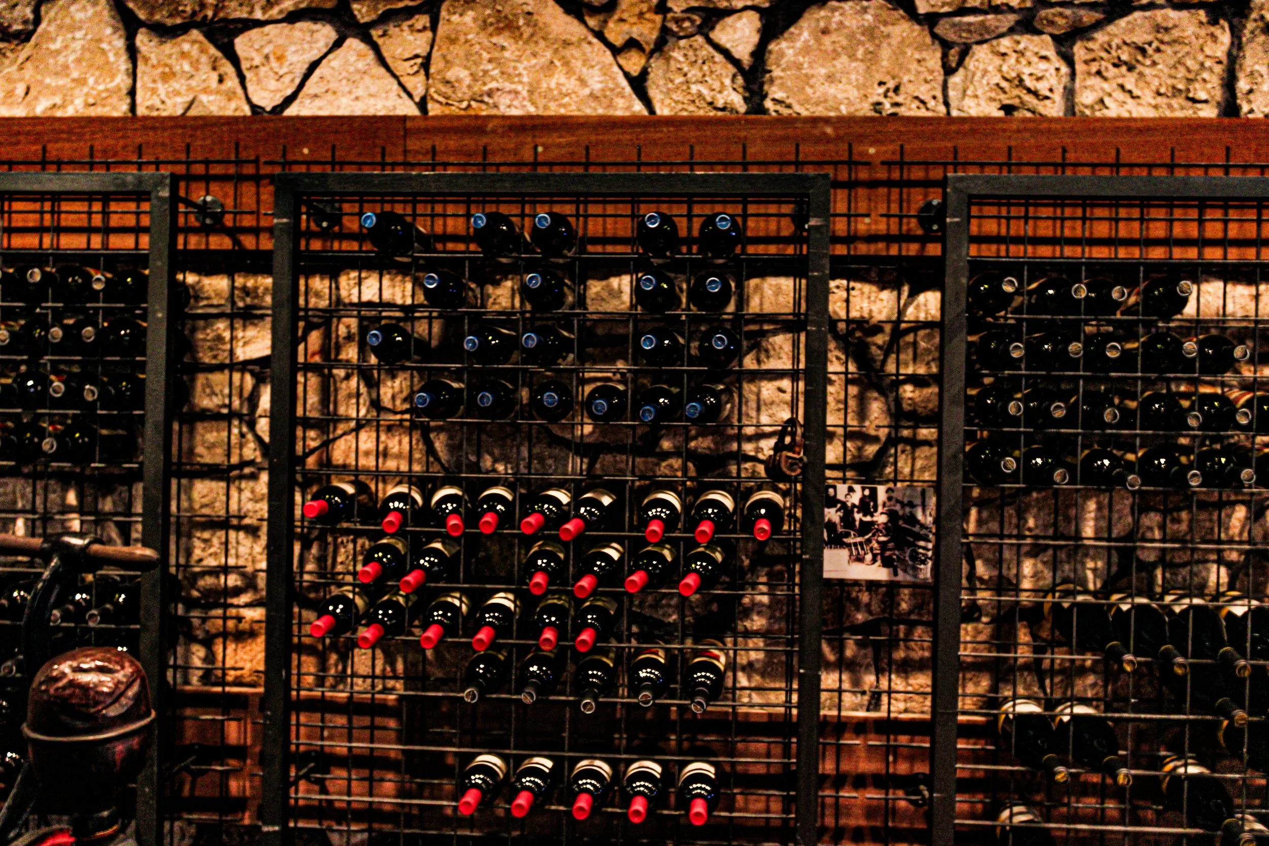 Wall-mounted wine rack with multiple bottles of wine, set against a stone and wood background.