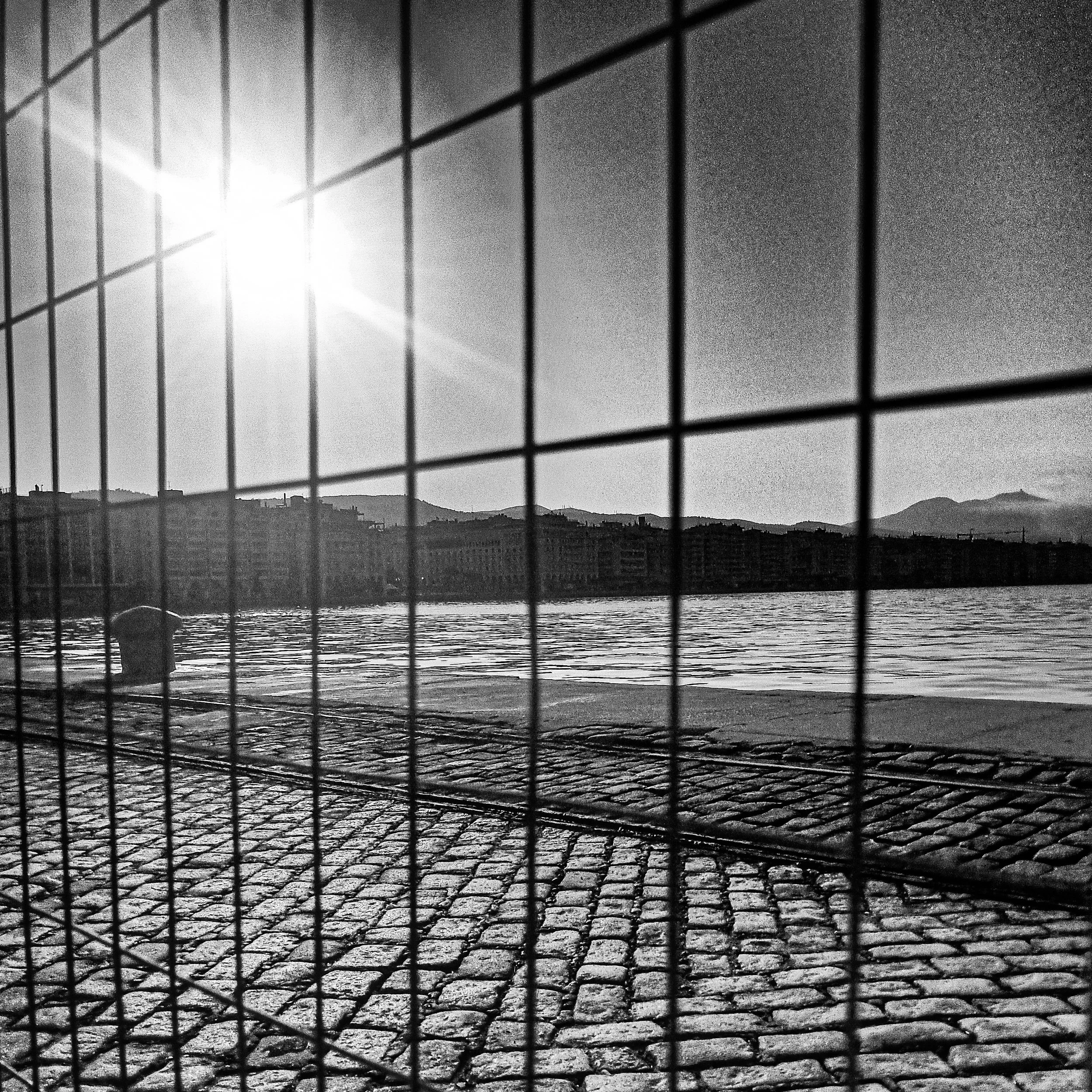 View of a city skyline and hills through a wire fence with bright sunlight