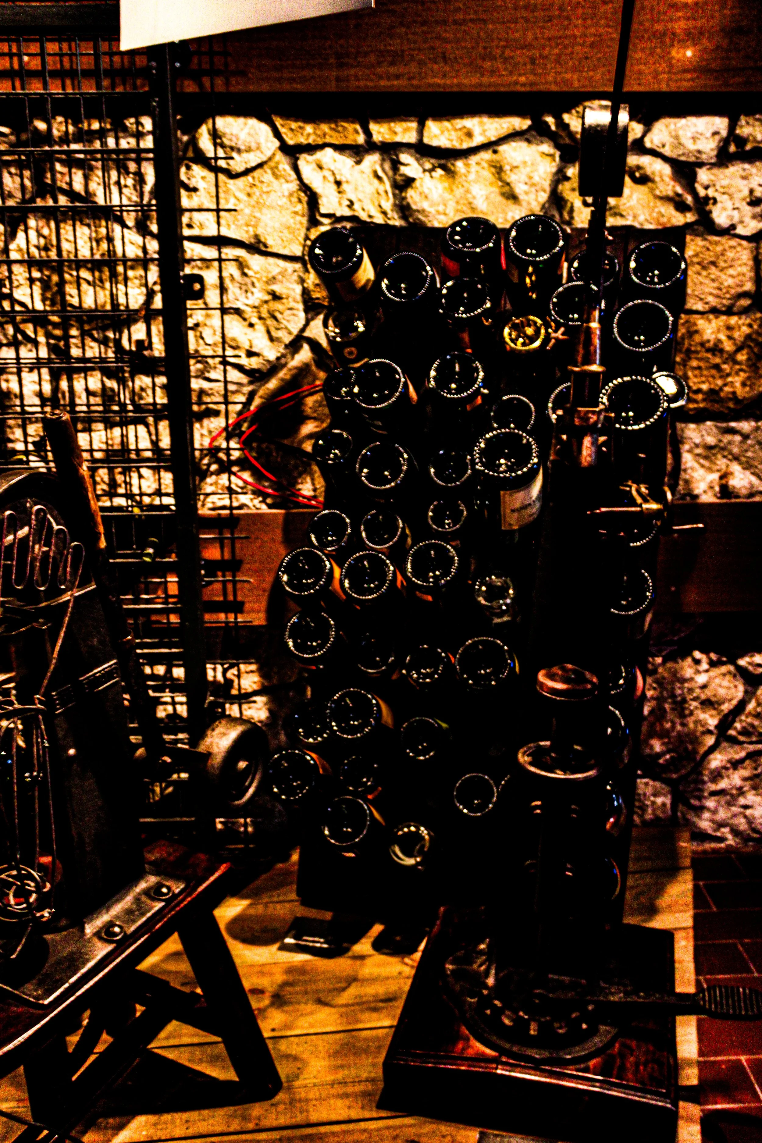 Bottle display with multiple bottles on a rack, set against a stone wall, in what appears to be a retail or bar setting.