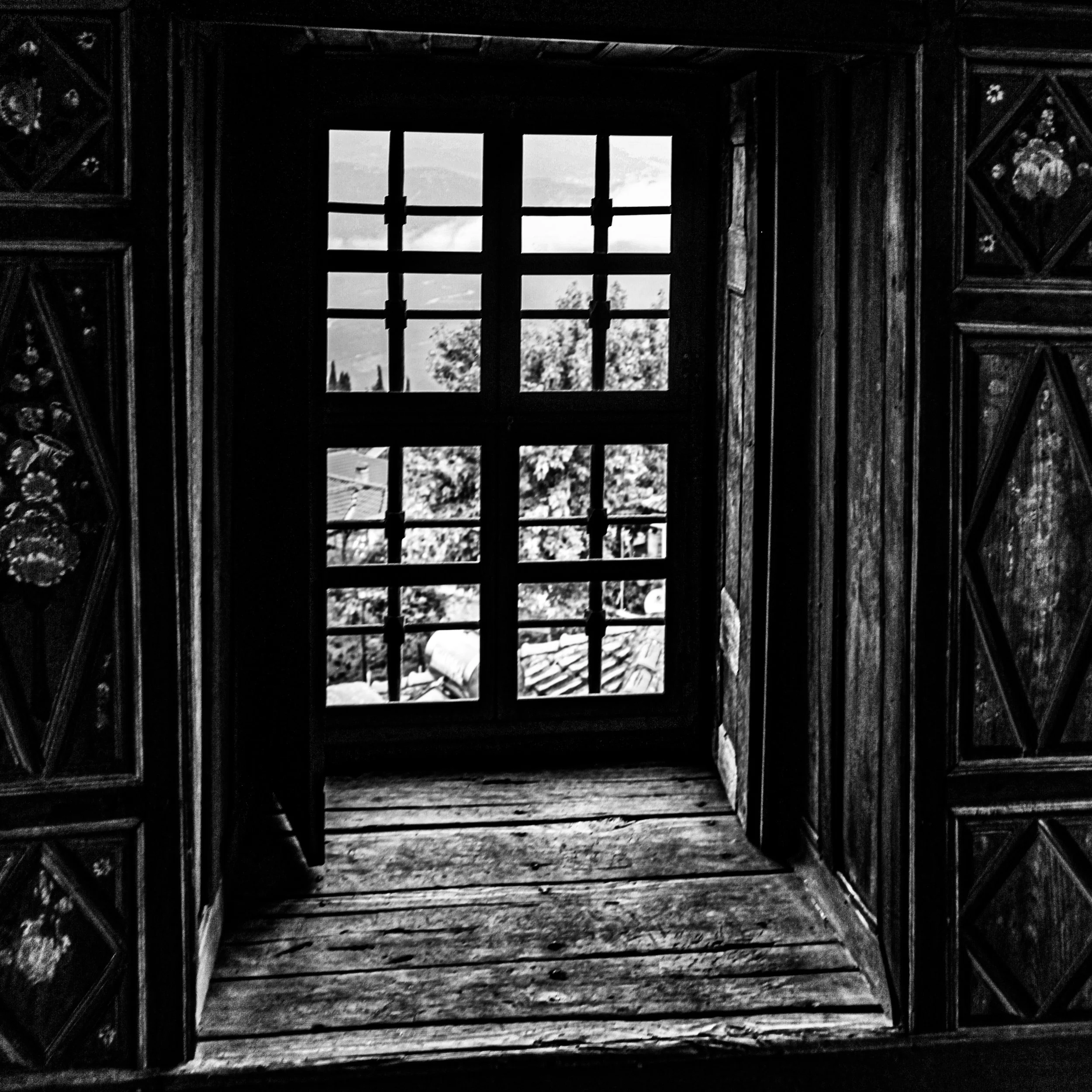 Black and white photo of a wooden structure with a window showing cloudy sky and trees outside.