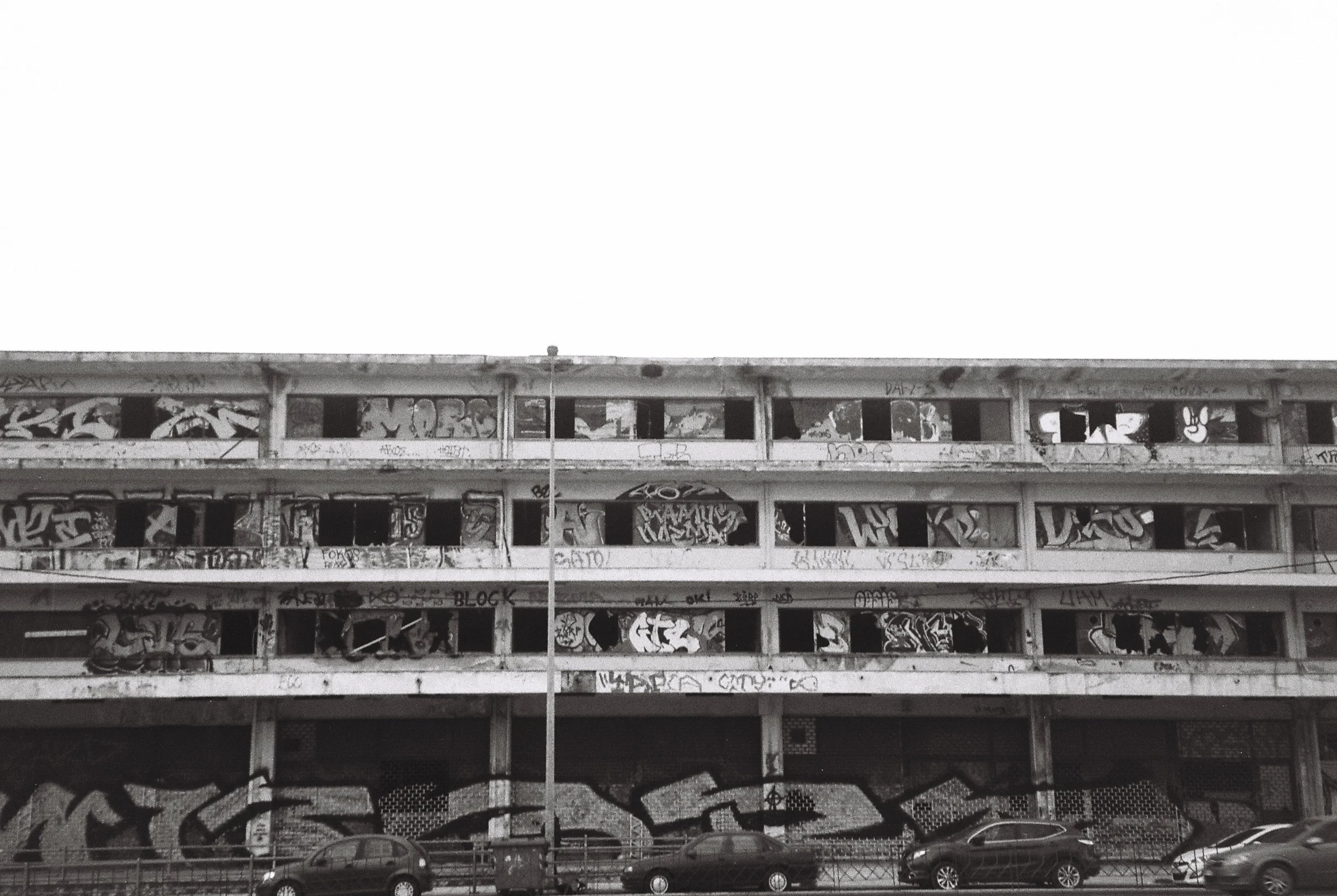 An abandoned, graffiti-covered building with four floors, parked cars in front, and a streetlamp in the foreground.