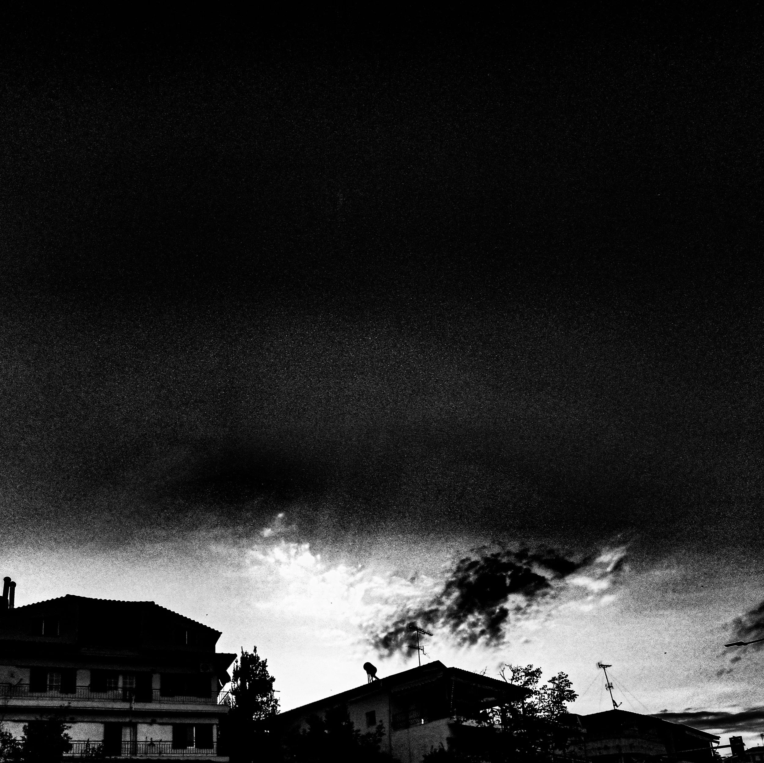 Black-and-white photo of rooftops, houses, and trees under a cloudy sky, with visible stars and a faint moon.