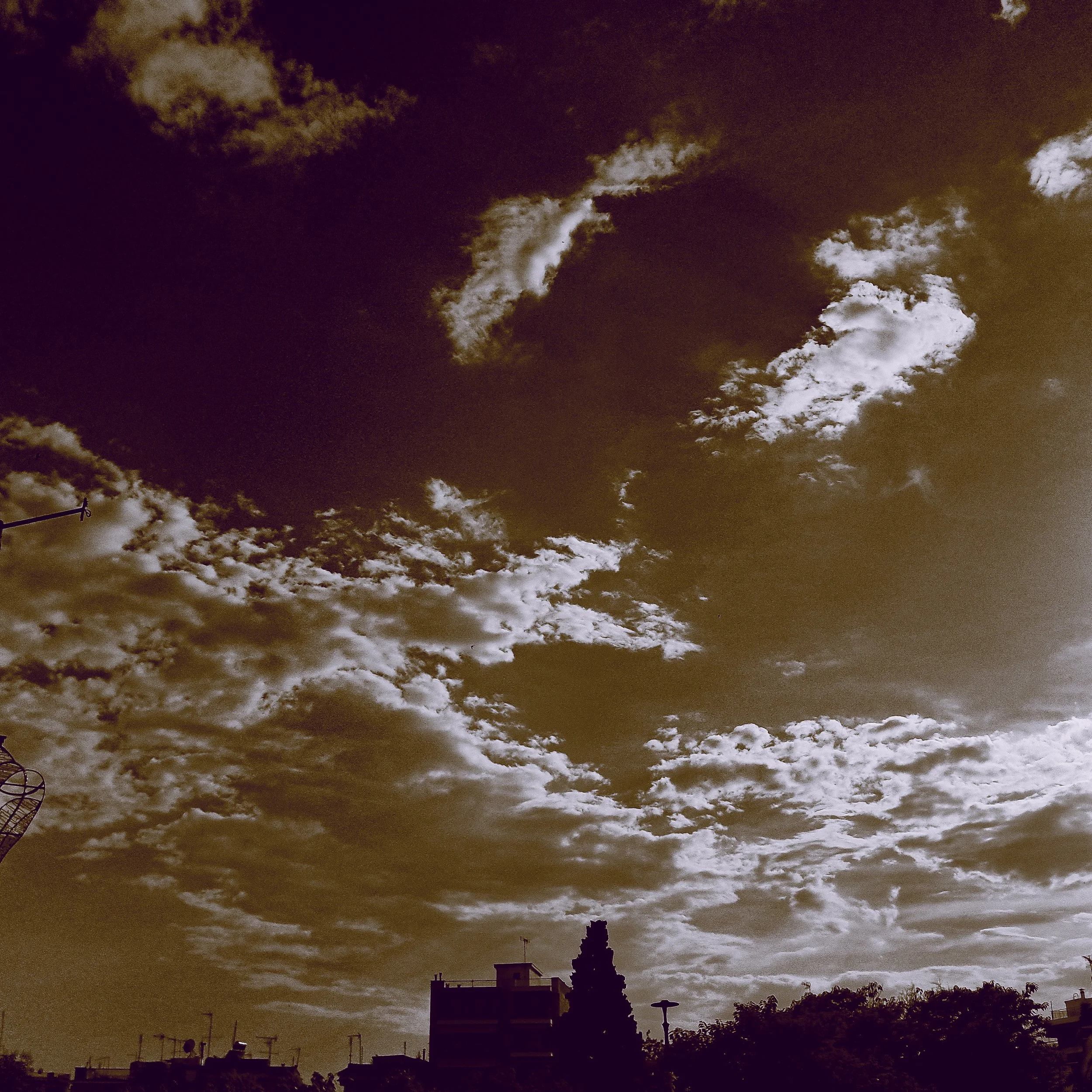 Nighttime cityscape with dark cliff and silhouette of buildings and trees, cloudy dark sky.