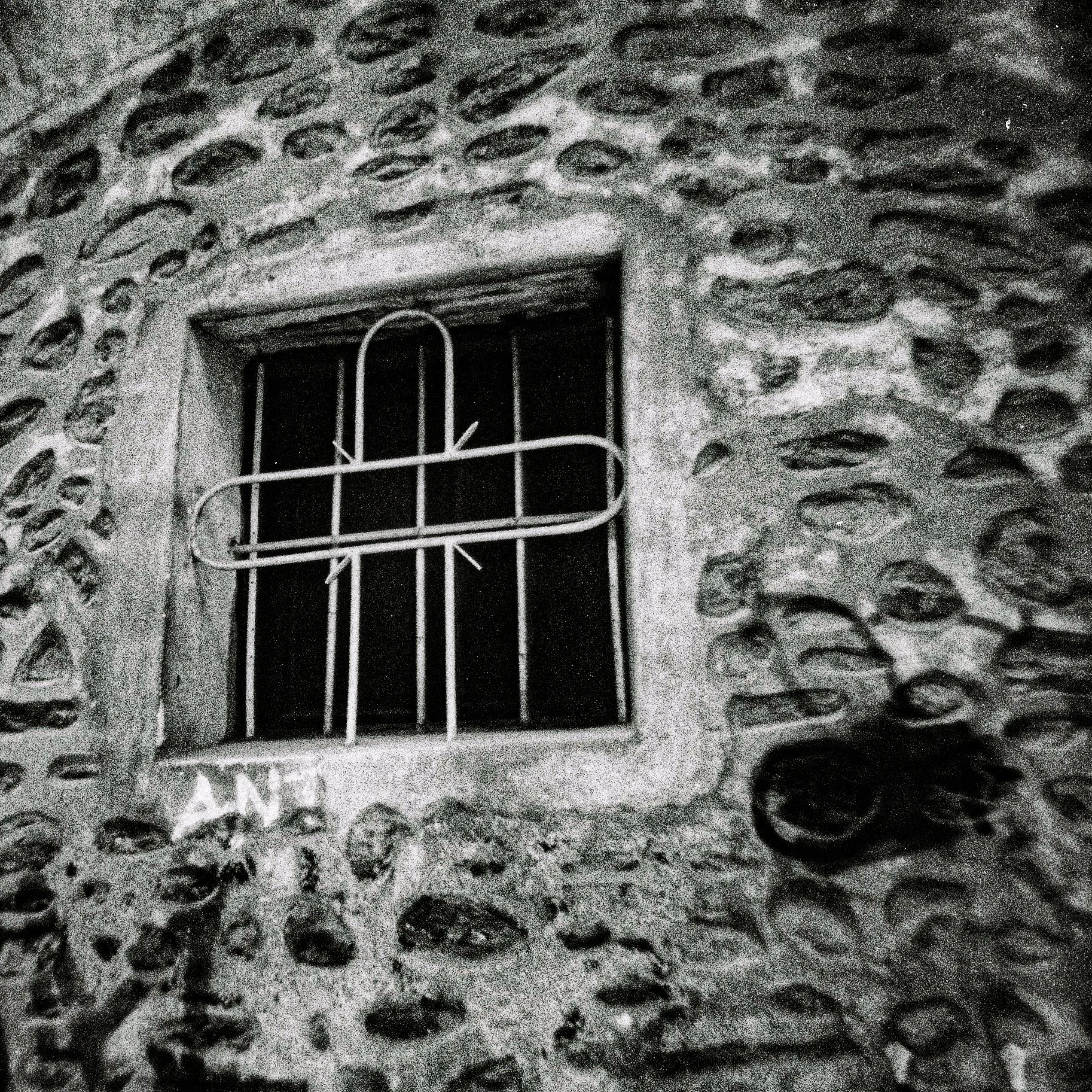 Close-up of a building with textured stone walls and a small window with a metal security grille.