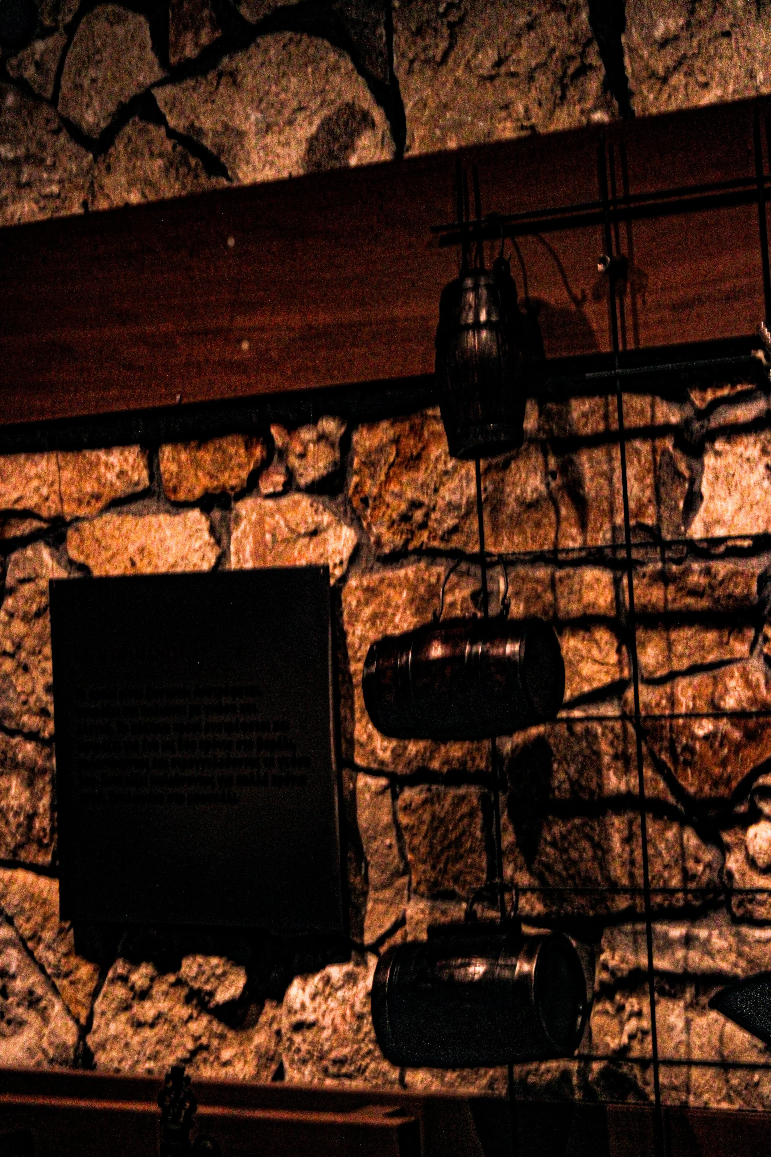 Close-up of a wall with a stone pattern, featuring a black wire grid and hanging black lantern-style lights.