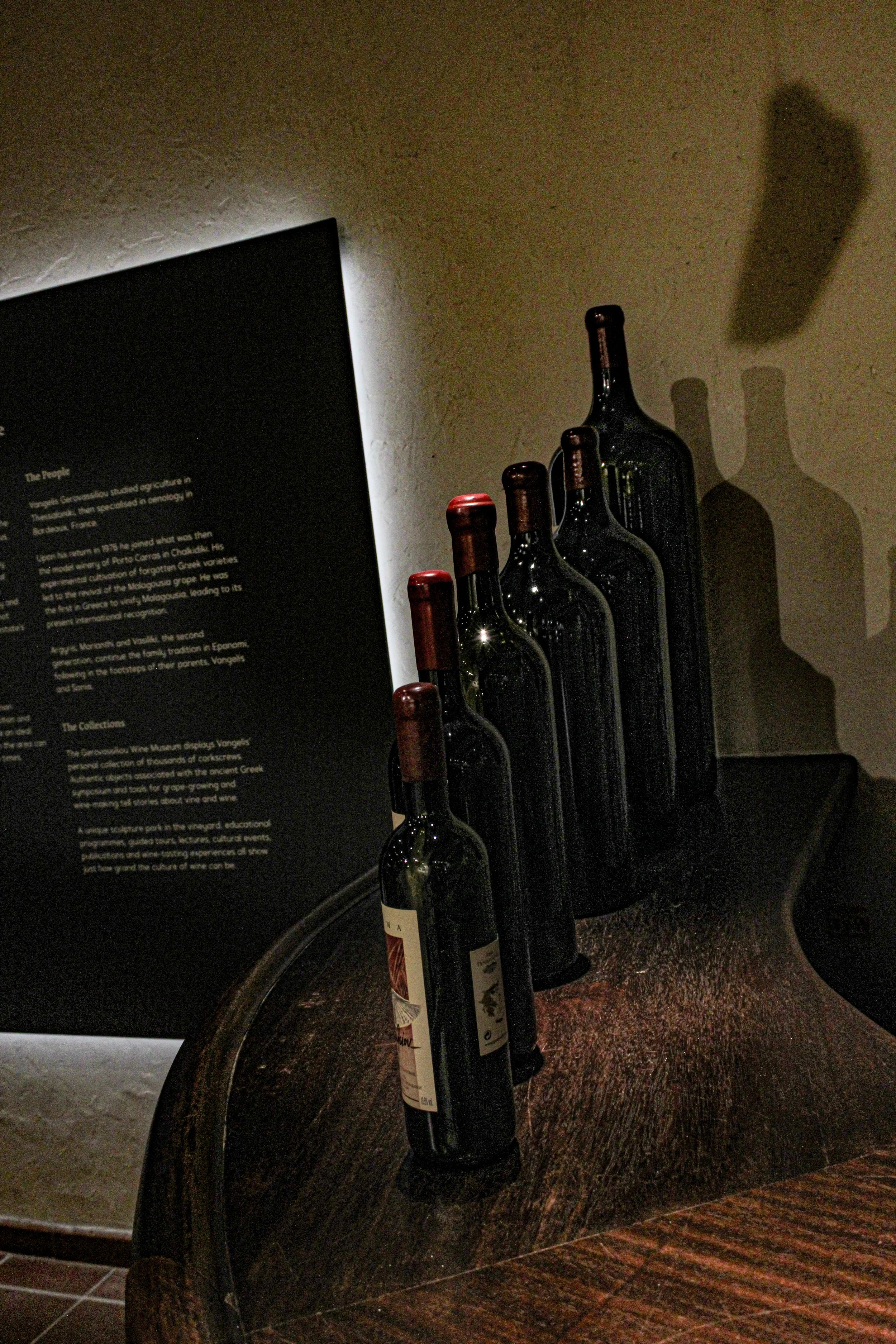 Several empty glass wine bottles on a dark wooden surface with a black informational display in the background, partially visible.