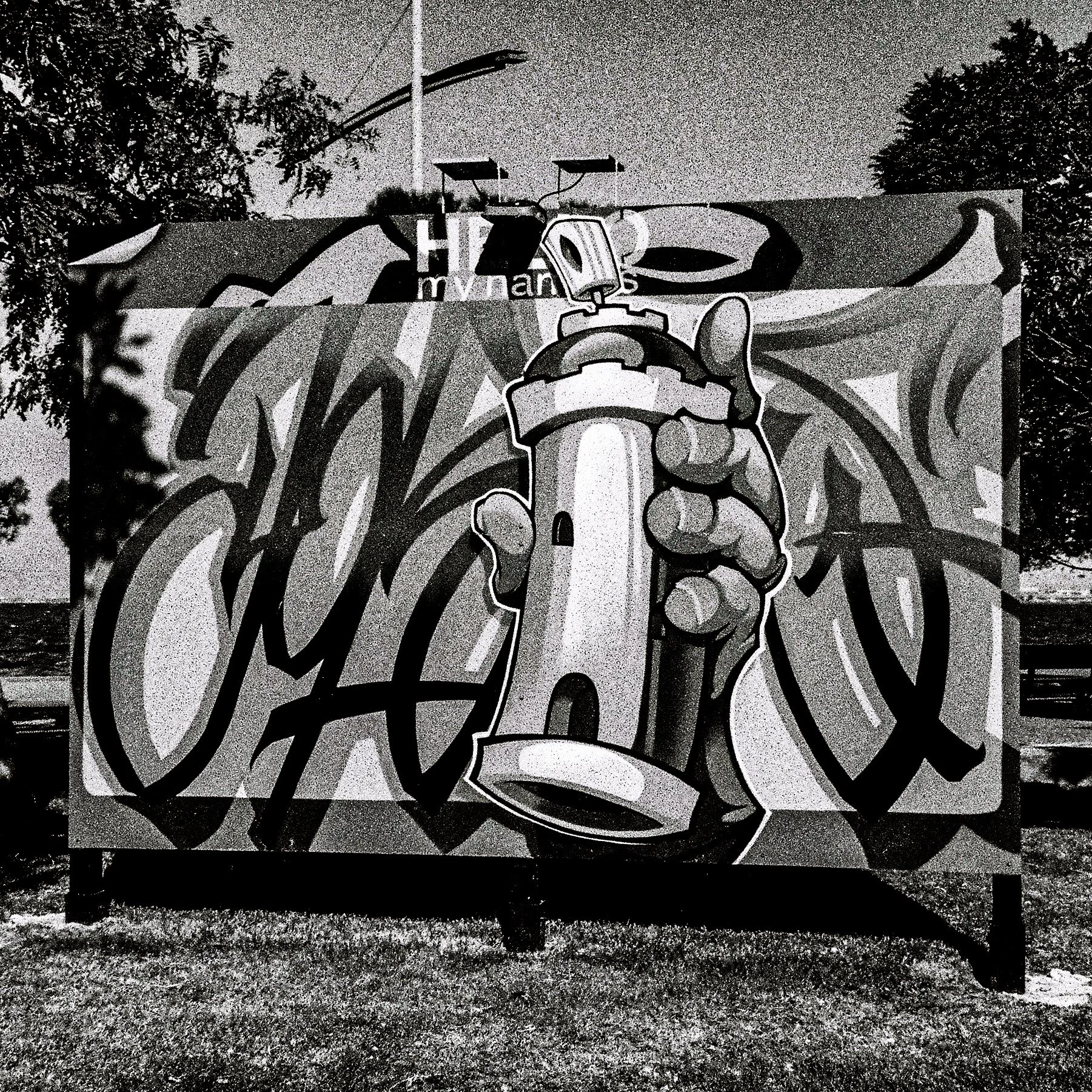 A black and white graffiti mural featuring a chef's hand holding a knife with a salad, set against a cityscape background with trees and a streetlamp.