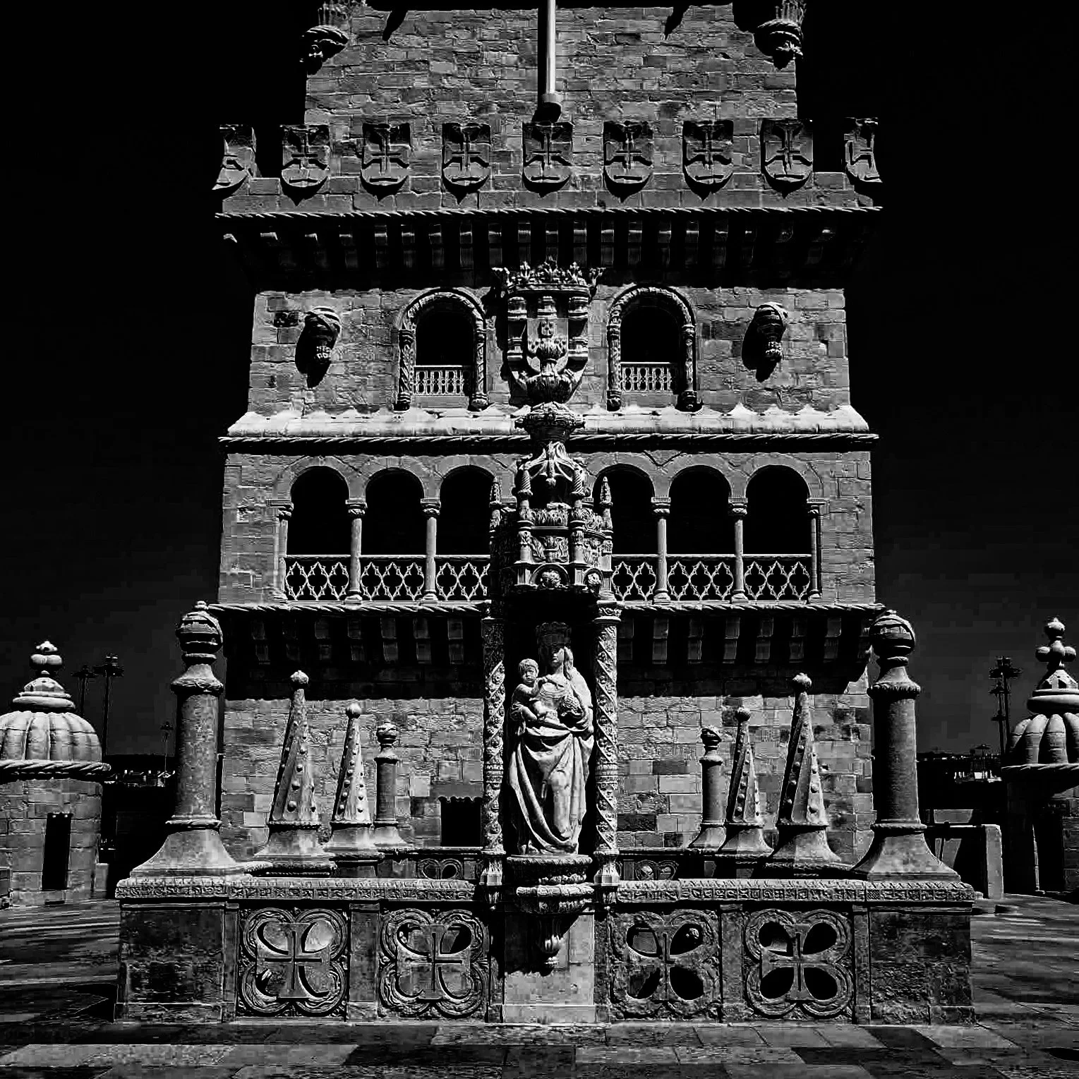 A historic stone building with ornate architectural details, including statues, balconies, and shields on the facade, illuminated against a dark night sky.