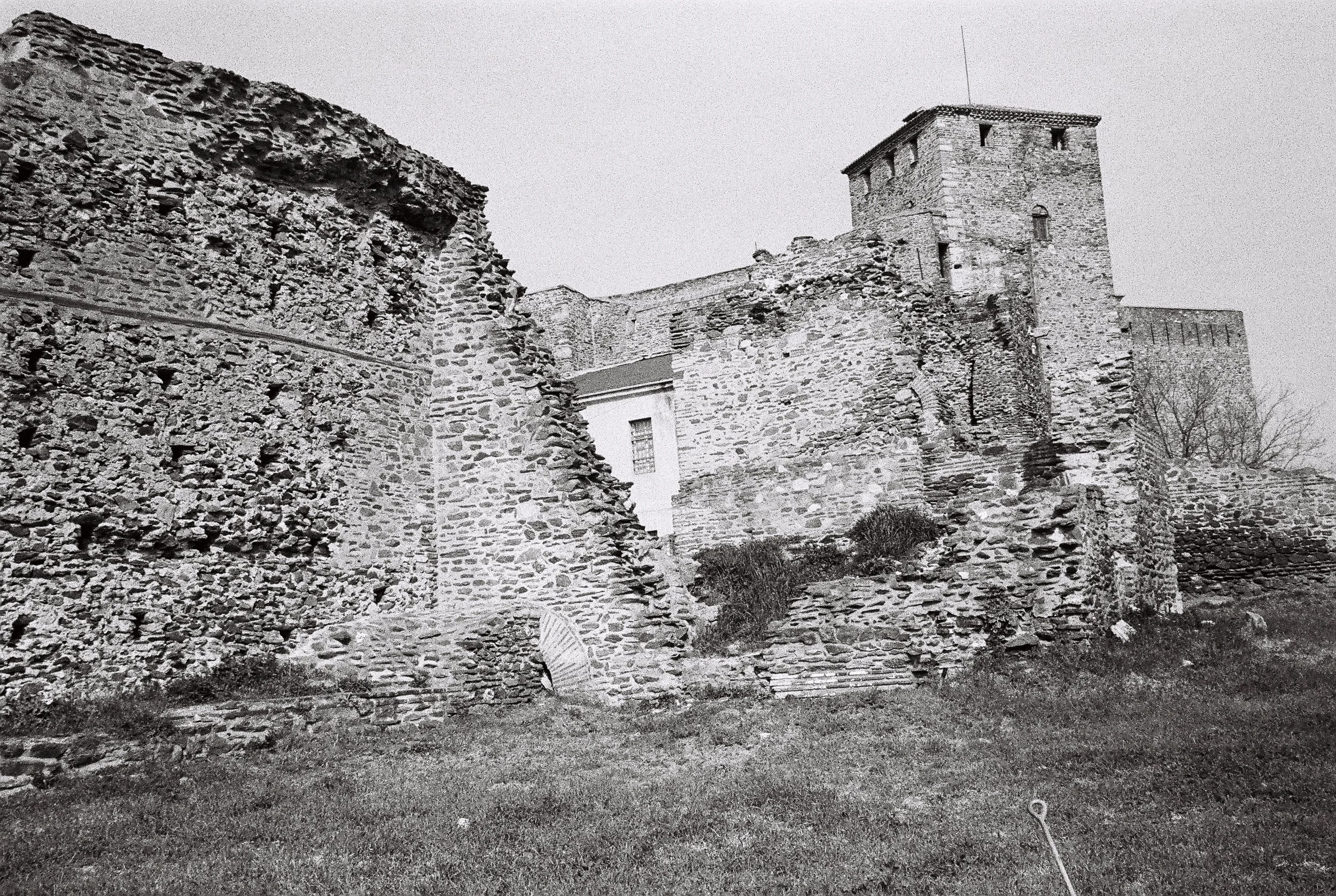 Black and white photo of ancient stone castle ruins with a stone tower, crumbling walls, and a grassy foreground.