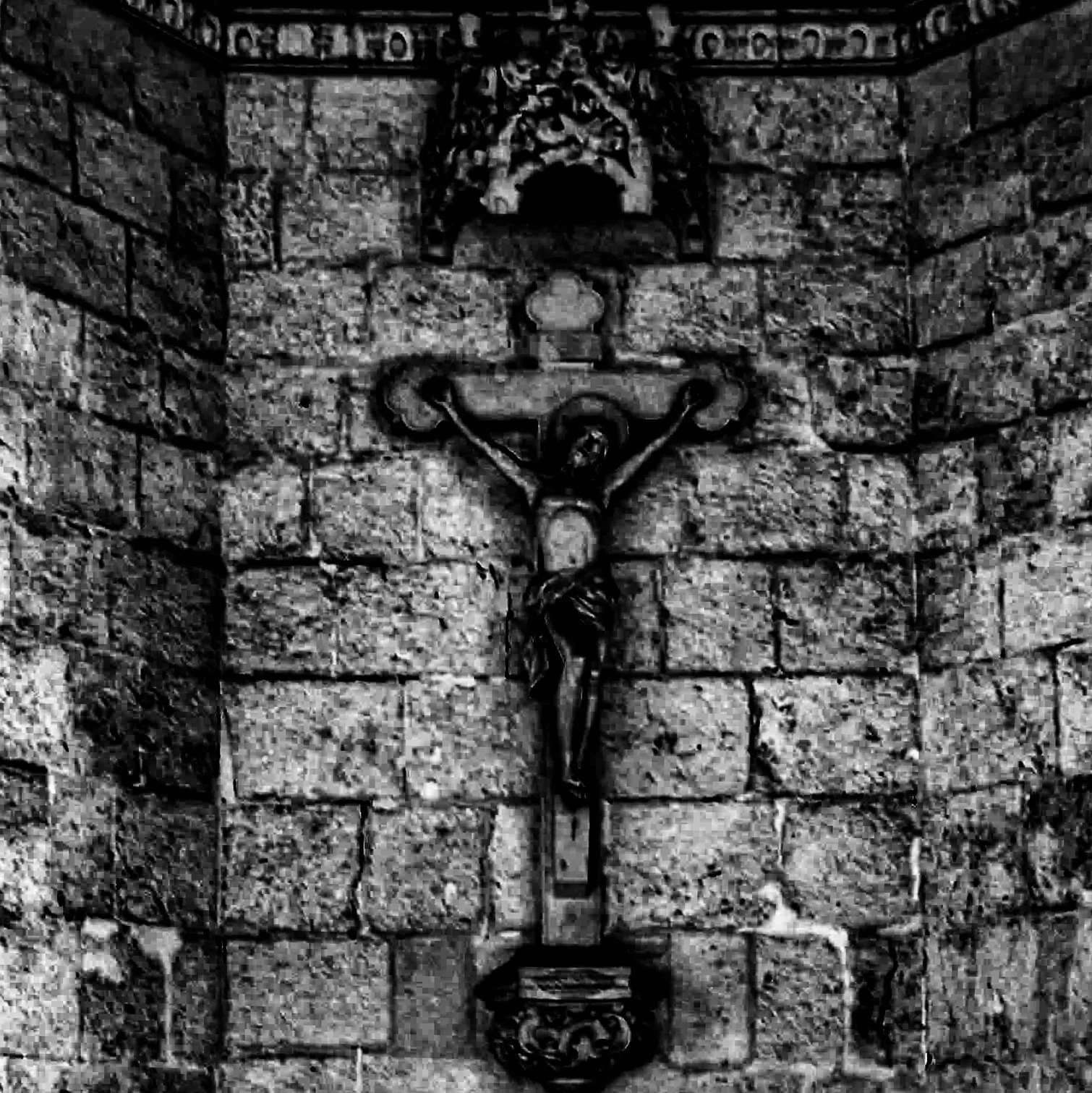 A black and white photograph of a stone wall with a decorative metal cross affixed to it.
