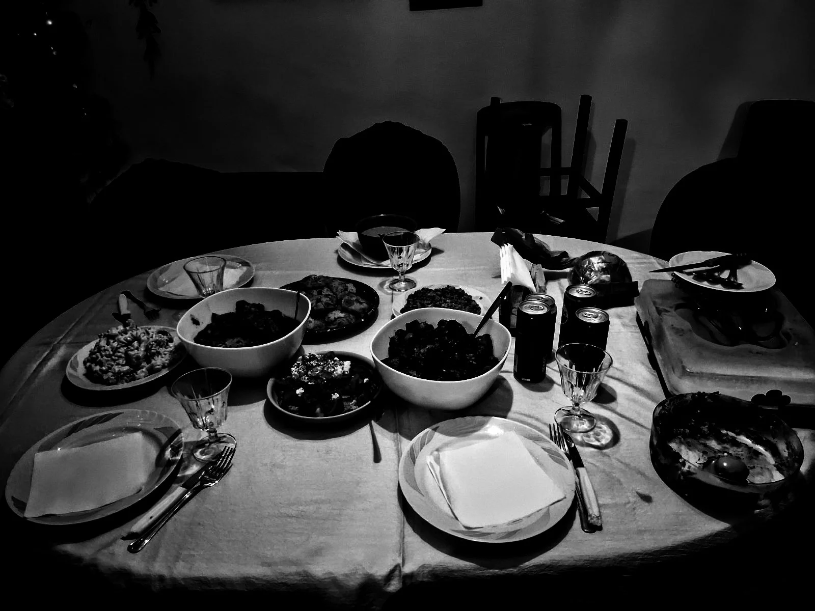 A round dining table set for a meal with various dishes, bowls, glasses, utensils, and empty plates. The scene is in a dimly lit room.