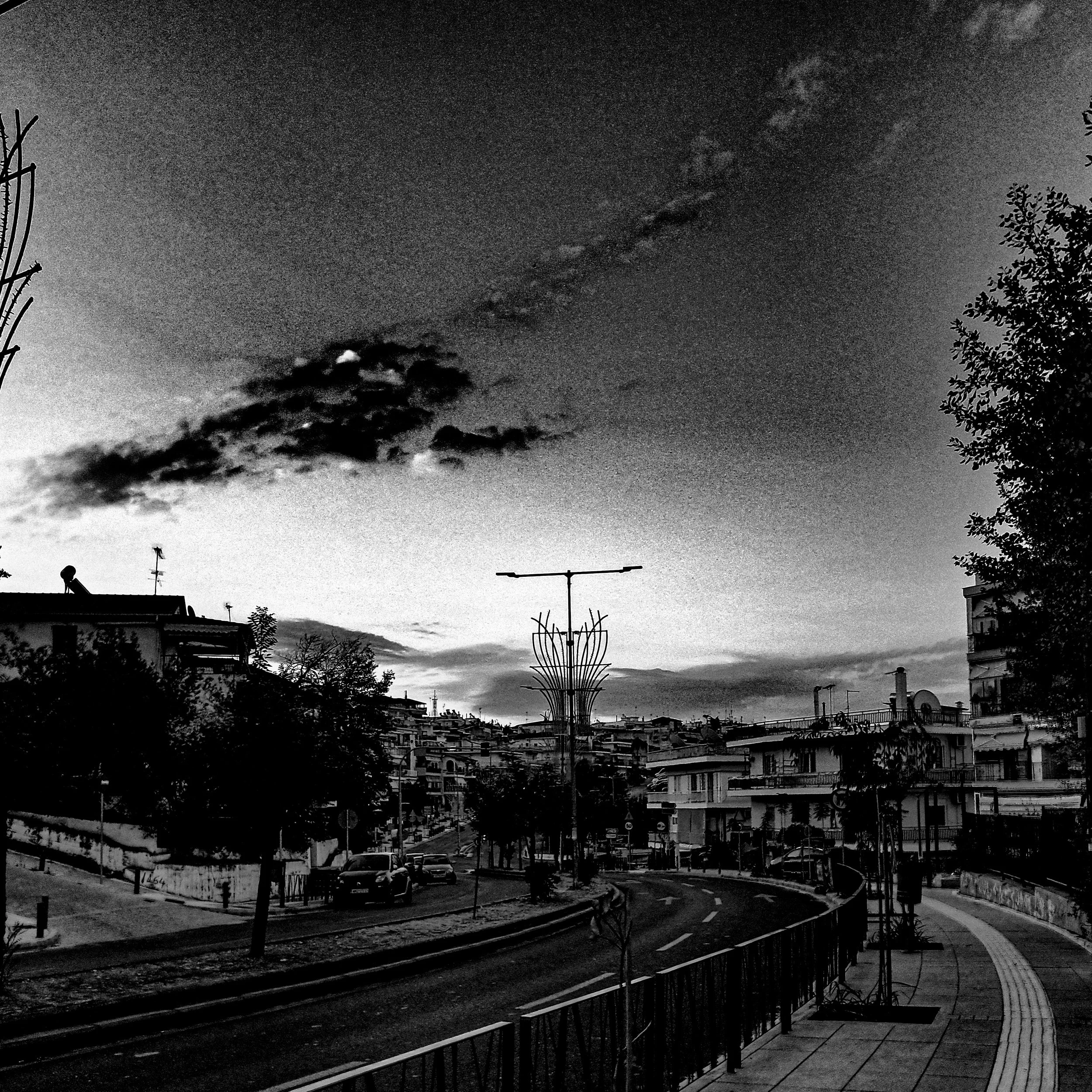 Nighttime cityscape with buildings, trees, and streetlights, black and white photo.