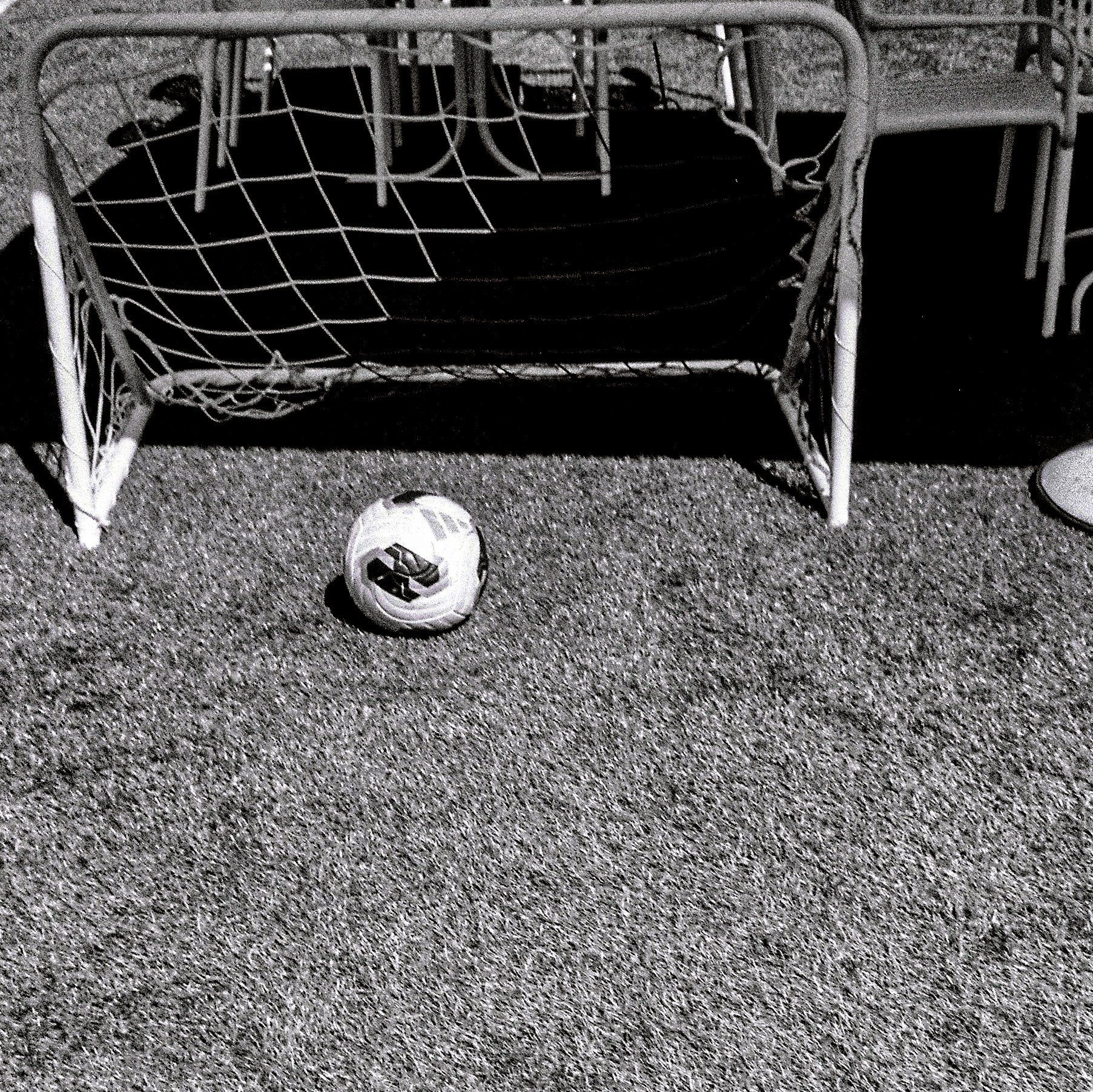 A soccer ball and small goal on a textured outdoor surface, likely a soccer field or playground.