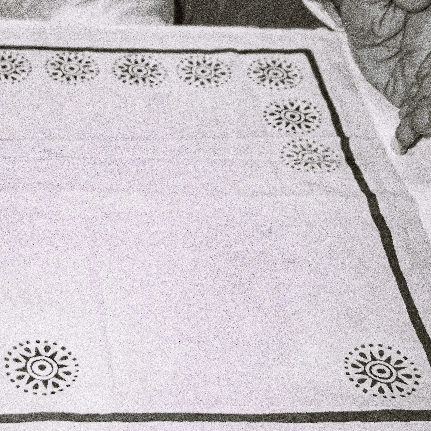 Close-up of a white paper surface with black decorative stamps arranged in a pattern, atop a textured fabric surface.