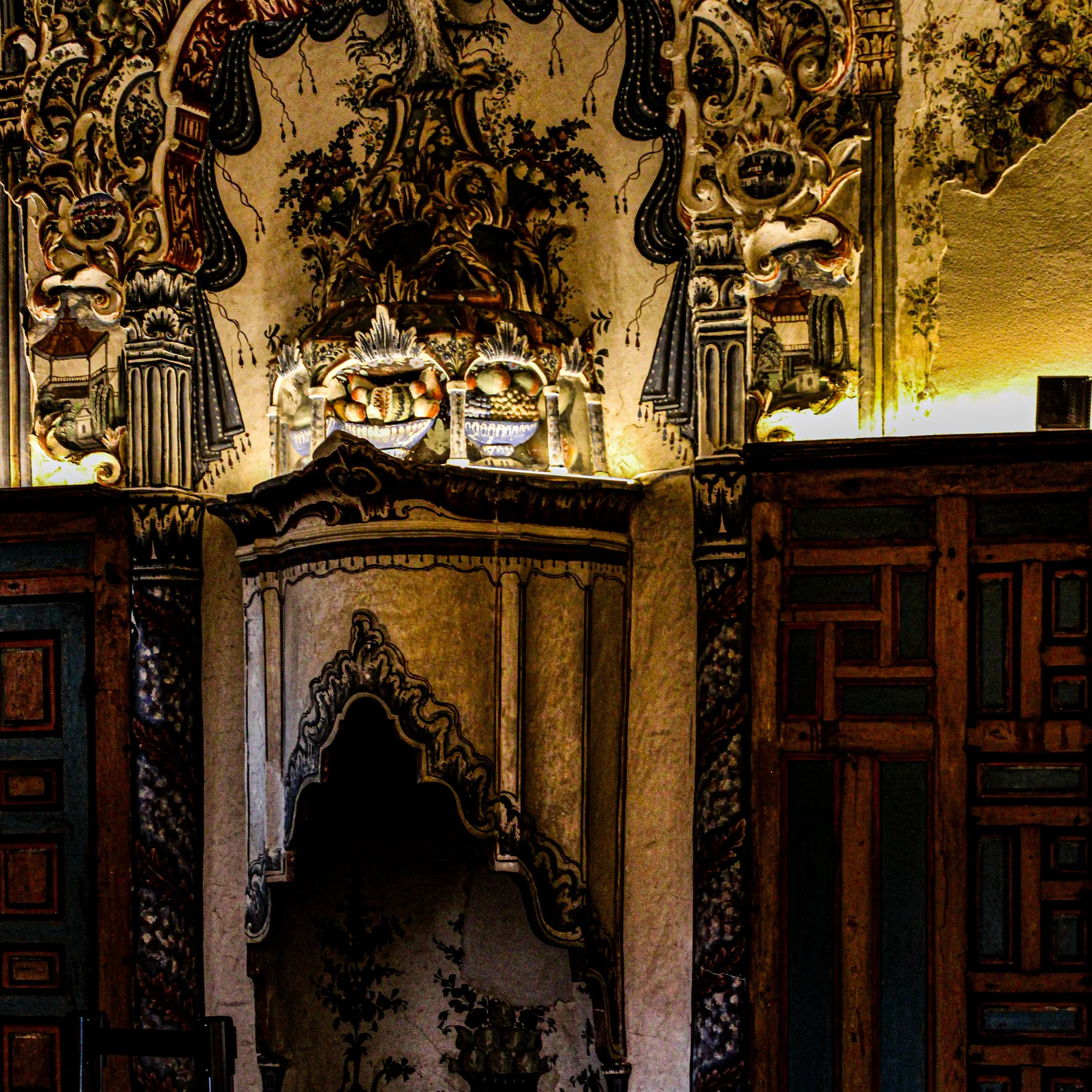 A detailed, ornate ceiling with elaborate decorative patterns, including floral motifs and intricate carvings, featuring a central chandelier with multiple elements.