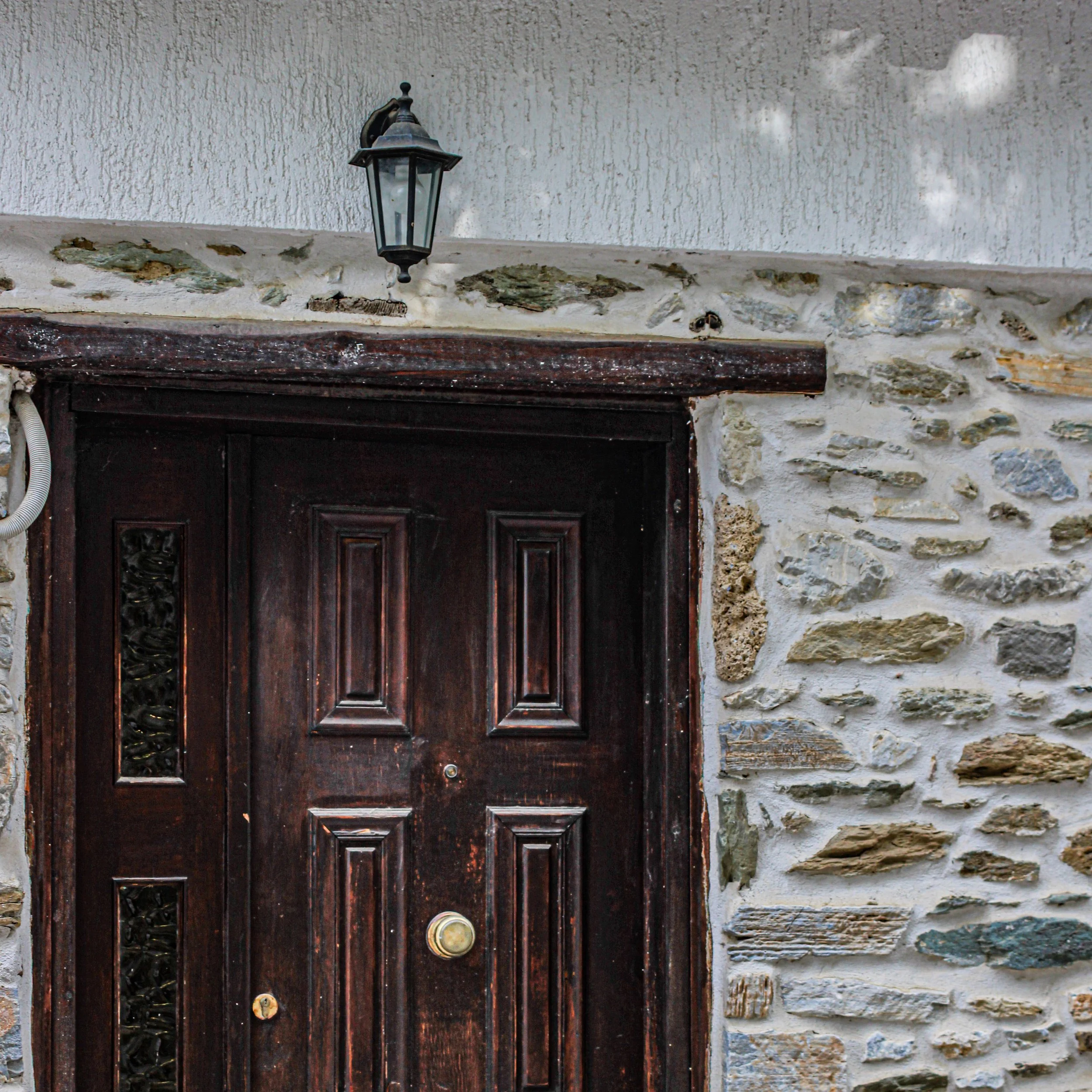 Close-up of a dark wooden front door with a textured stone wall and a black outdoor lantern mounted above the door