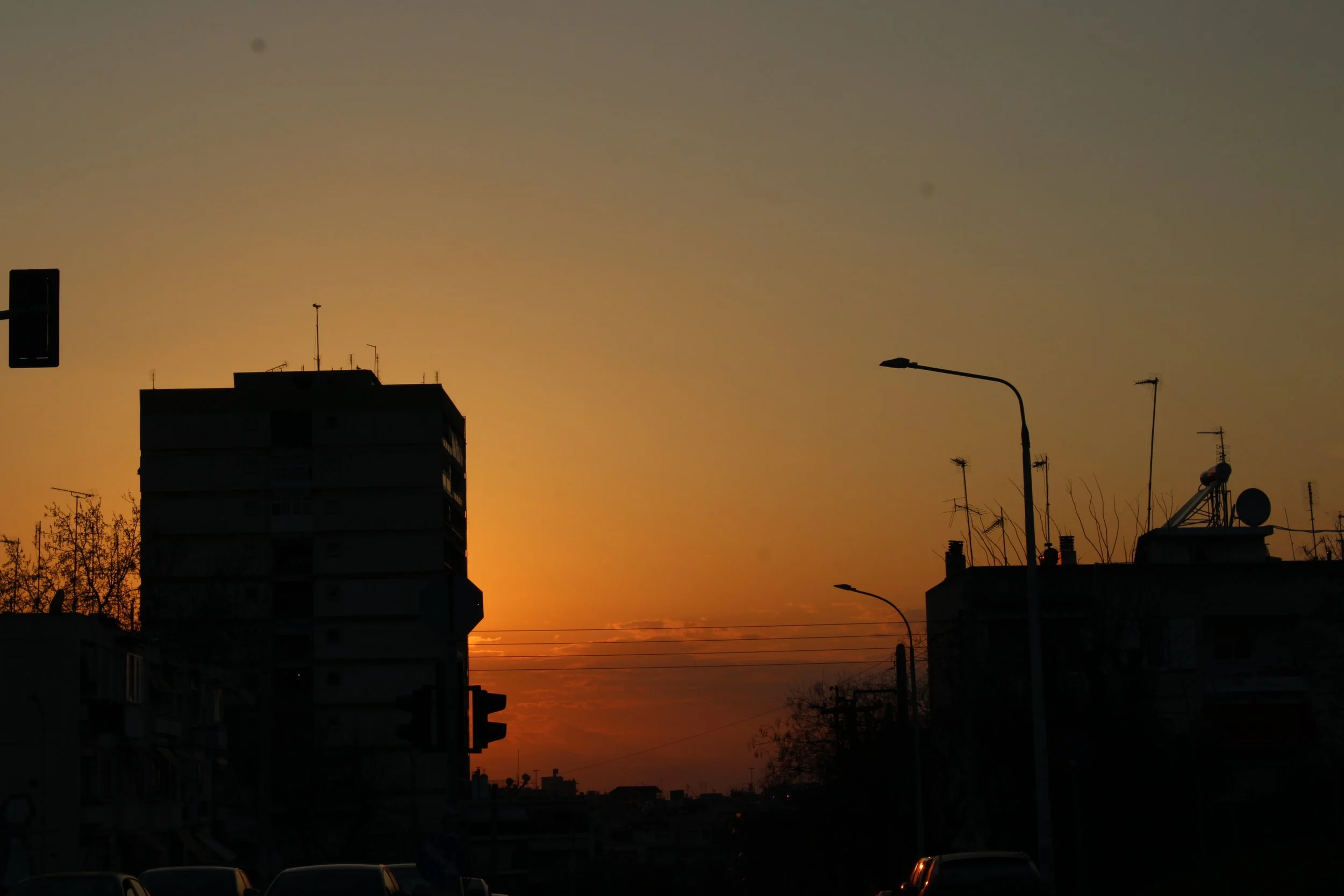 City skyline at sunset with silhouettes of buildings, streetlights, and antennas in the foreground.