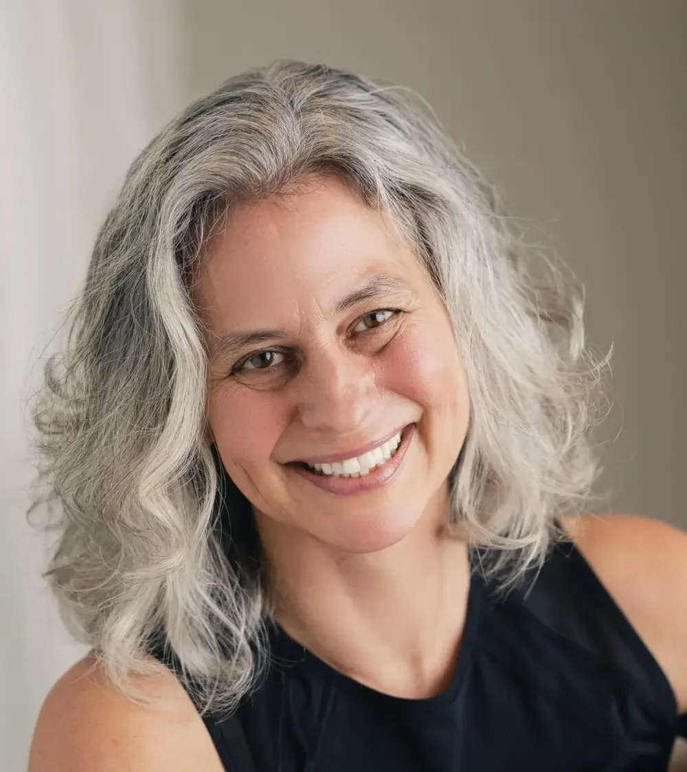 A smiling woman with shoulder-length gray hair wearing a black sleeveless top