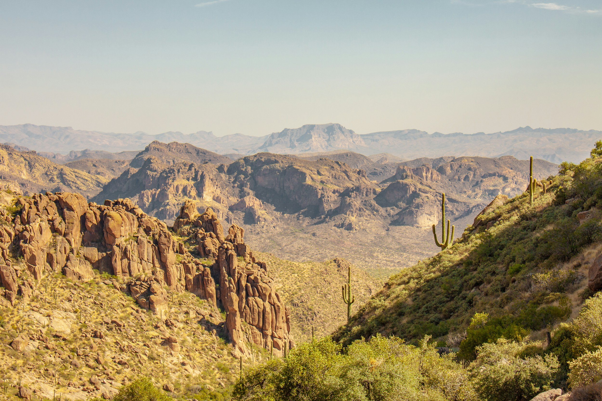 A desert landscape with rocky mountains, cacti, and sparse vegetation under a clear sky.