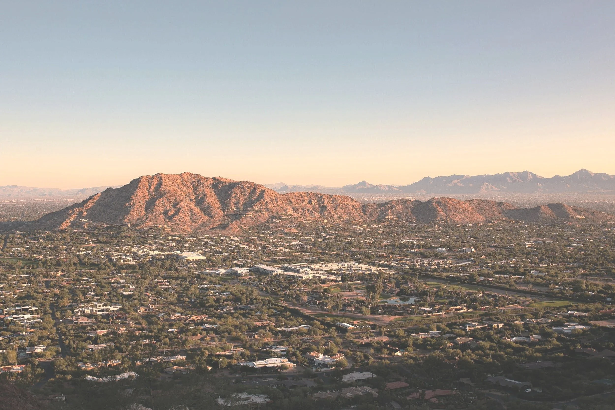 A scenic view of Tucson Arizona during sunrise, with a cityscape and residential area in the foreground.