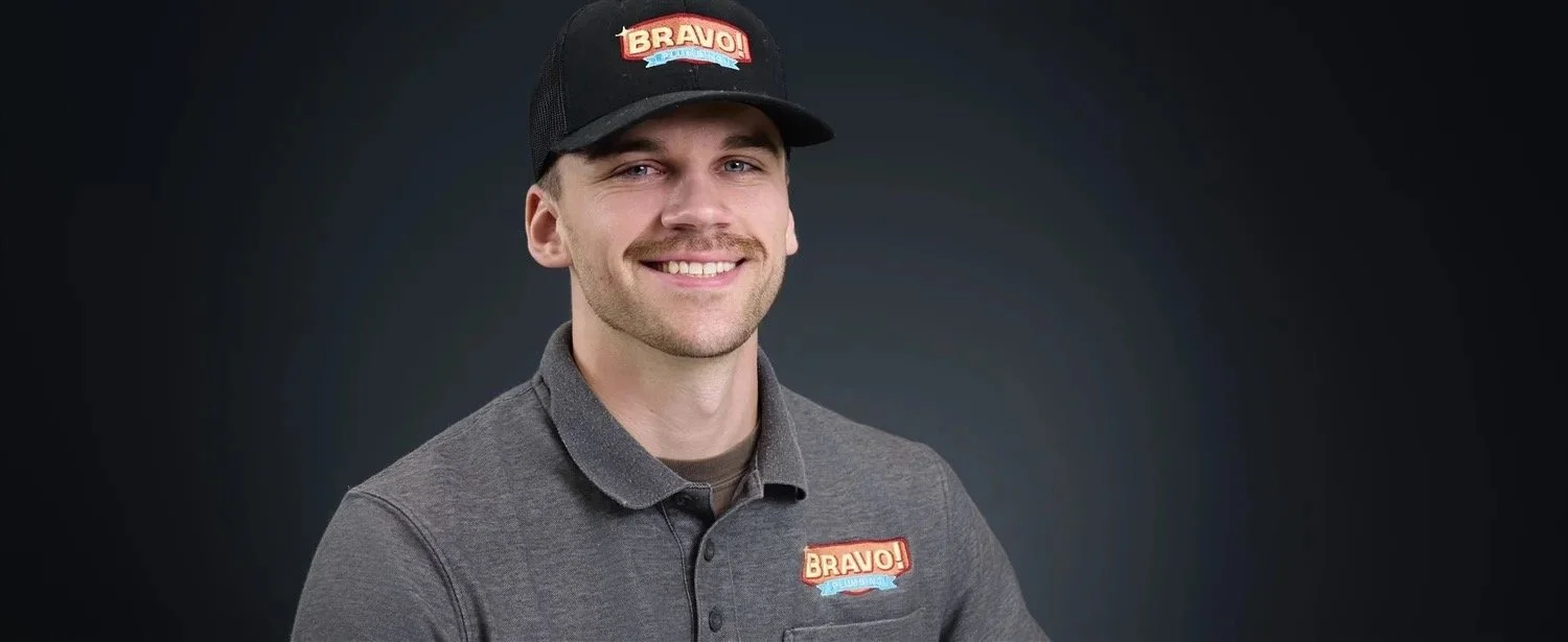 A KH Media Co Headshot of Young man smiling, wearing a gray polo shirt and a black cap with a red and white "Bravo!" logo.