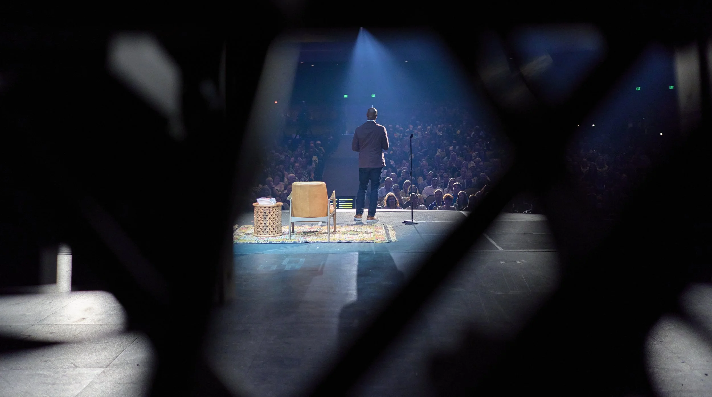 A performer standing on stage, facing an audience in a dark theater, viewed through a peephole or lattice.