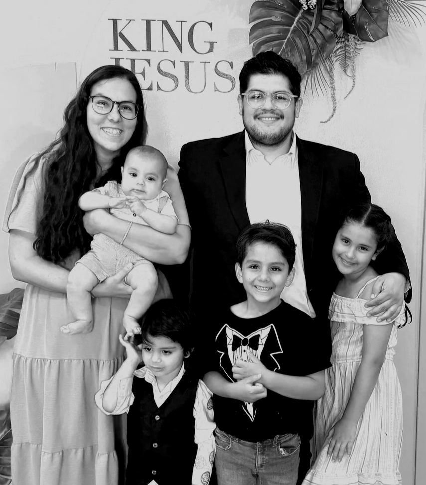 Family photo featuring a woman, a man, and four children posing in front of a wall with a religious message that says 'King Jesus.'