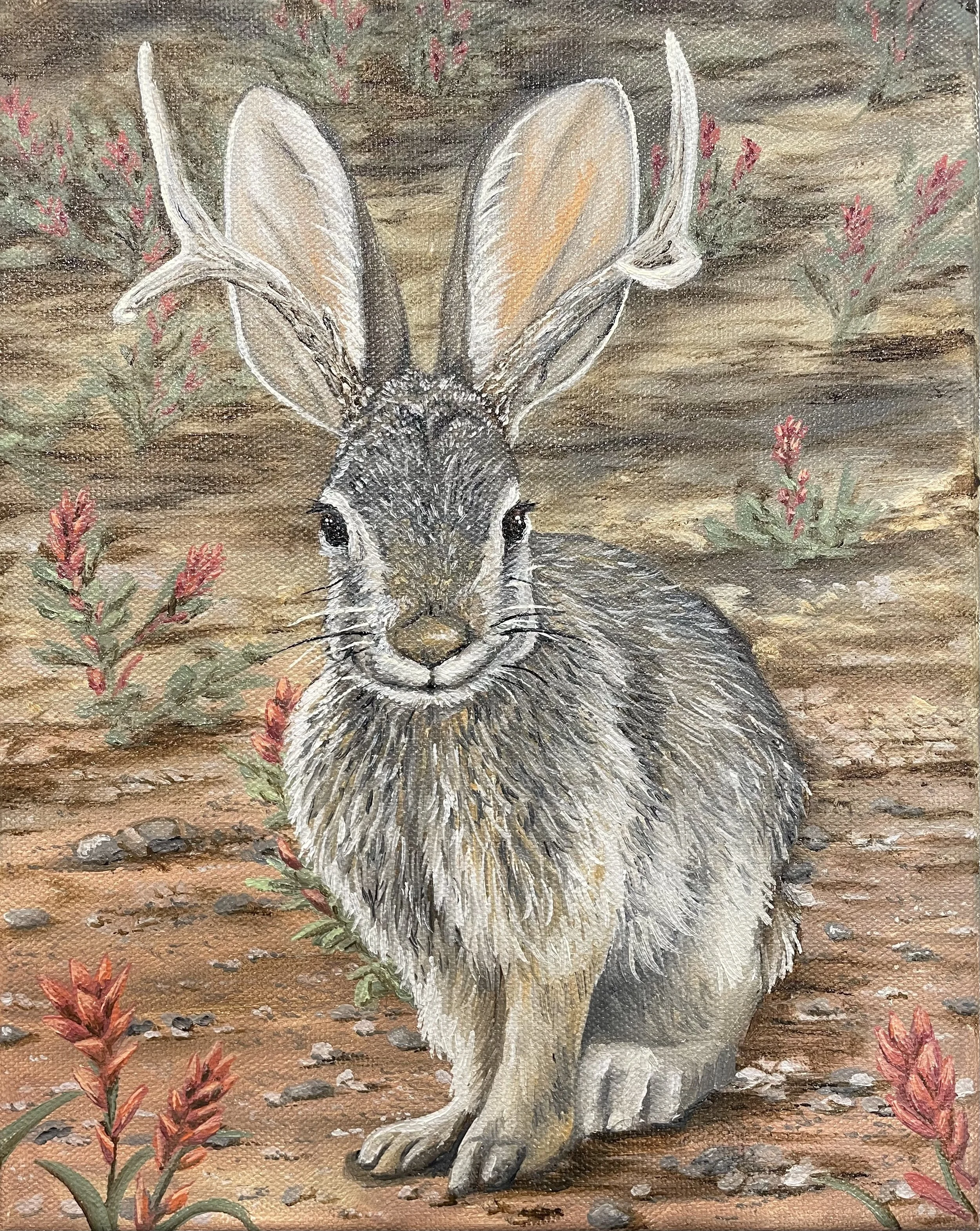 A realistic painting of a jackalope with white fur and black eyes, sitting on a brownish ground surrounded by small rocks and red and green plants, against a background of a blurred landscape with green, red, and brown colors.