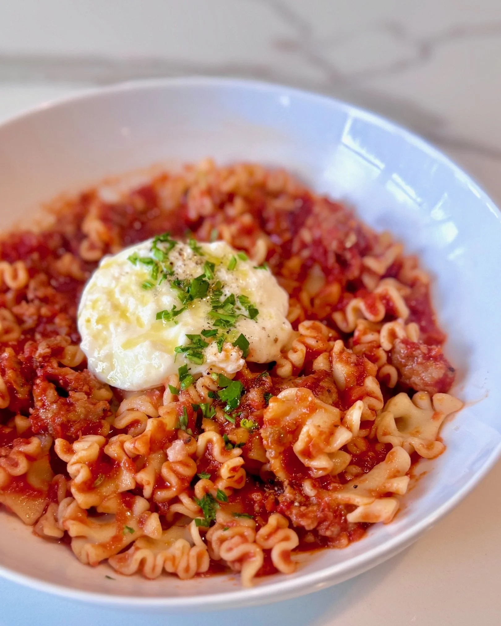 A white bowl filled with cooked rotini pasta topped with tomato sauce and garnished with chopped herbs and a poached egg.