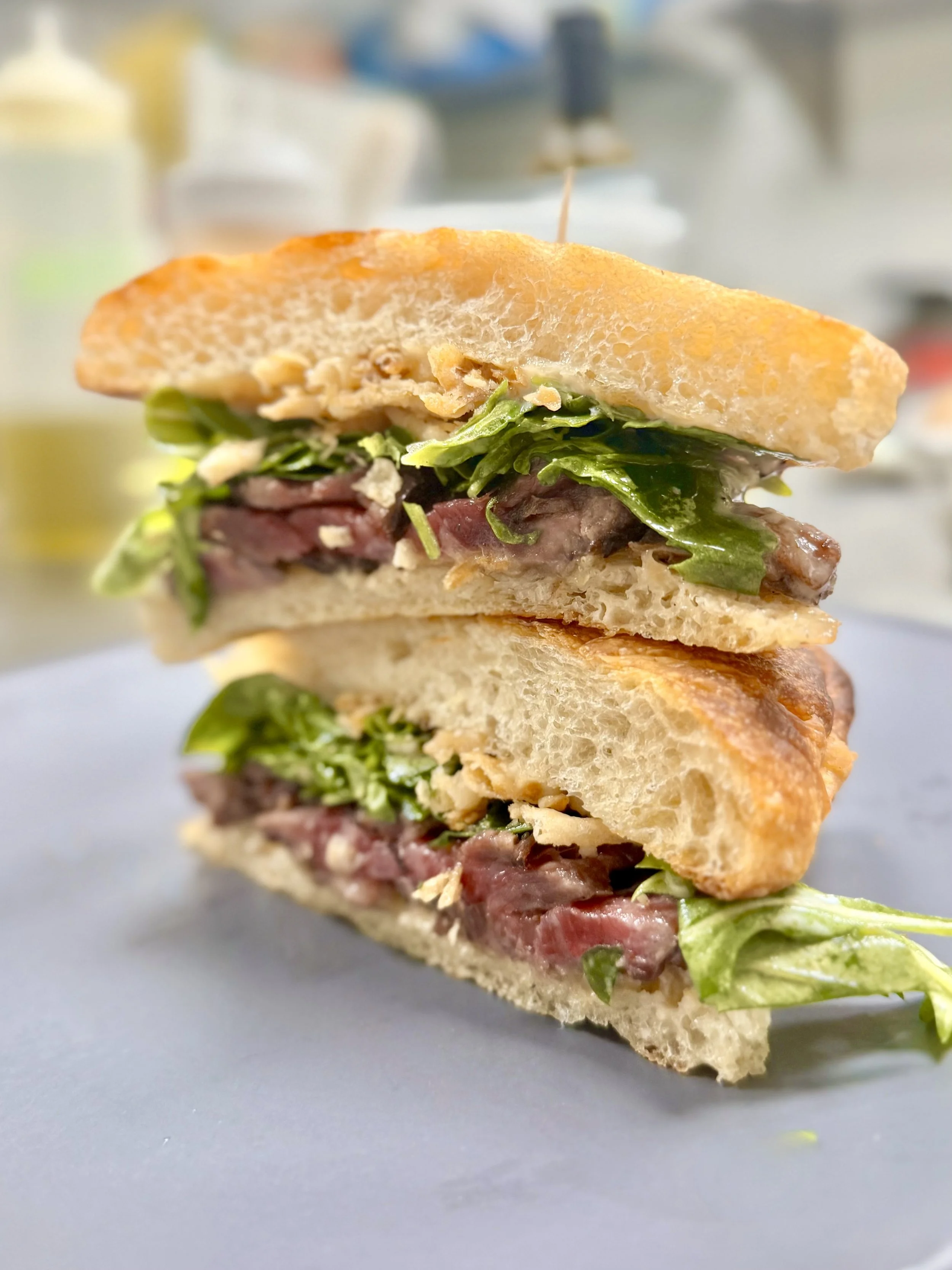 Close-up of a sliced sandwich with lettuce, red meat, and bread, placed on a gray surface.