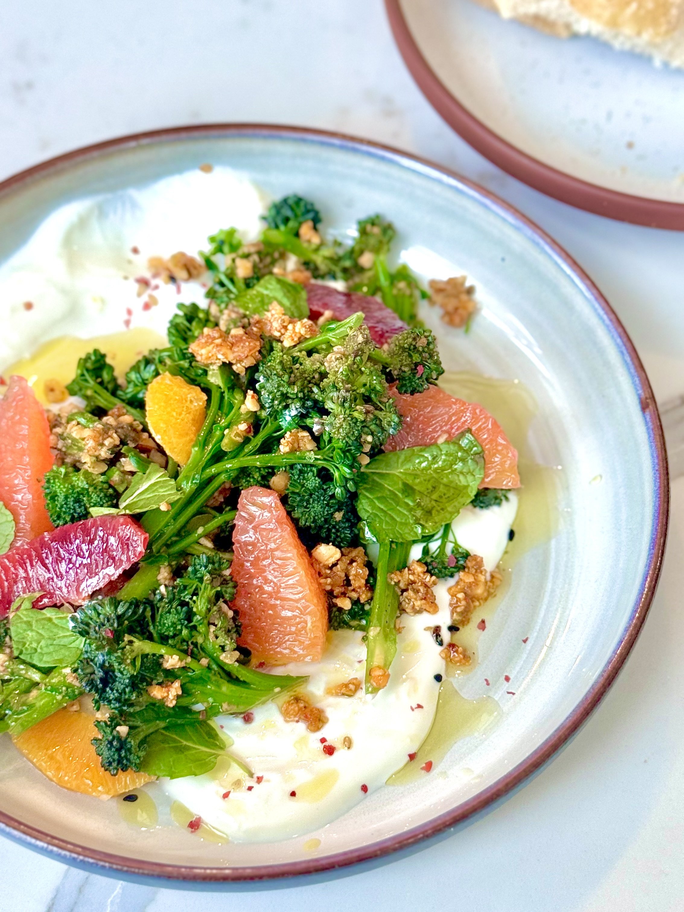 A bowl of salad with broccoli, grapefruit slices, and other vegetables with dressing and crushed nuts.