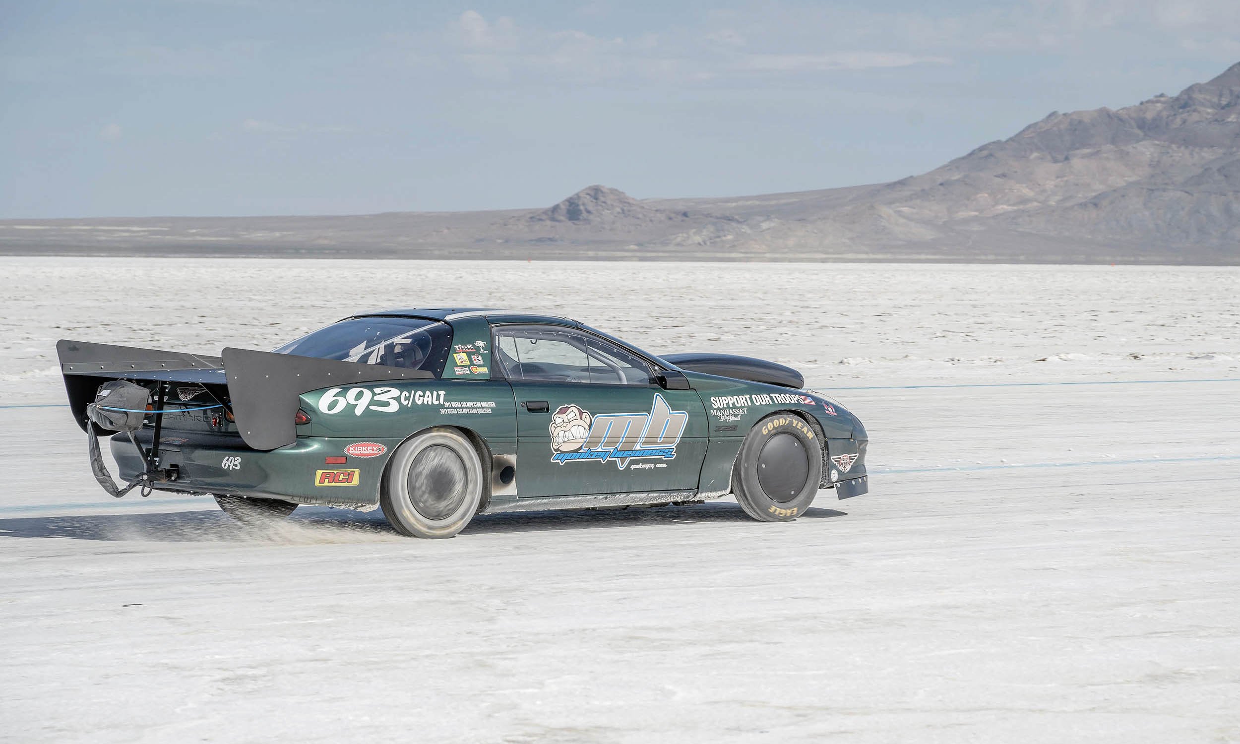 A race car speeding on a salt flat with mountains in the background.