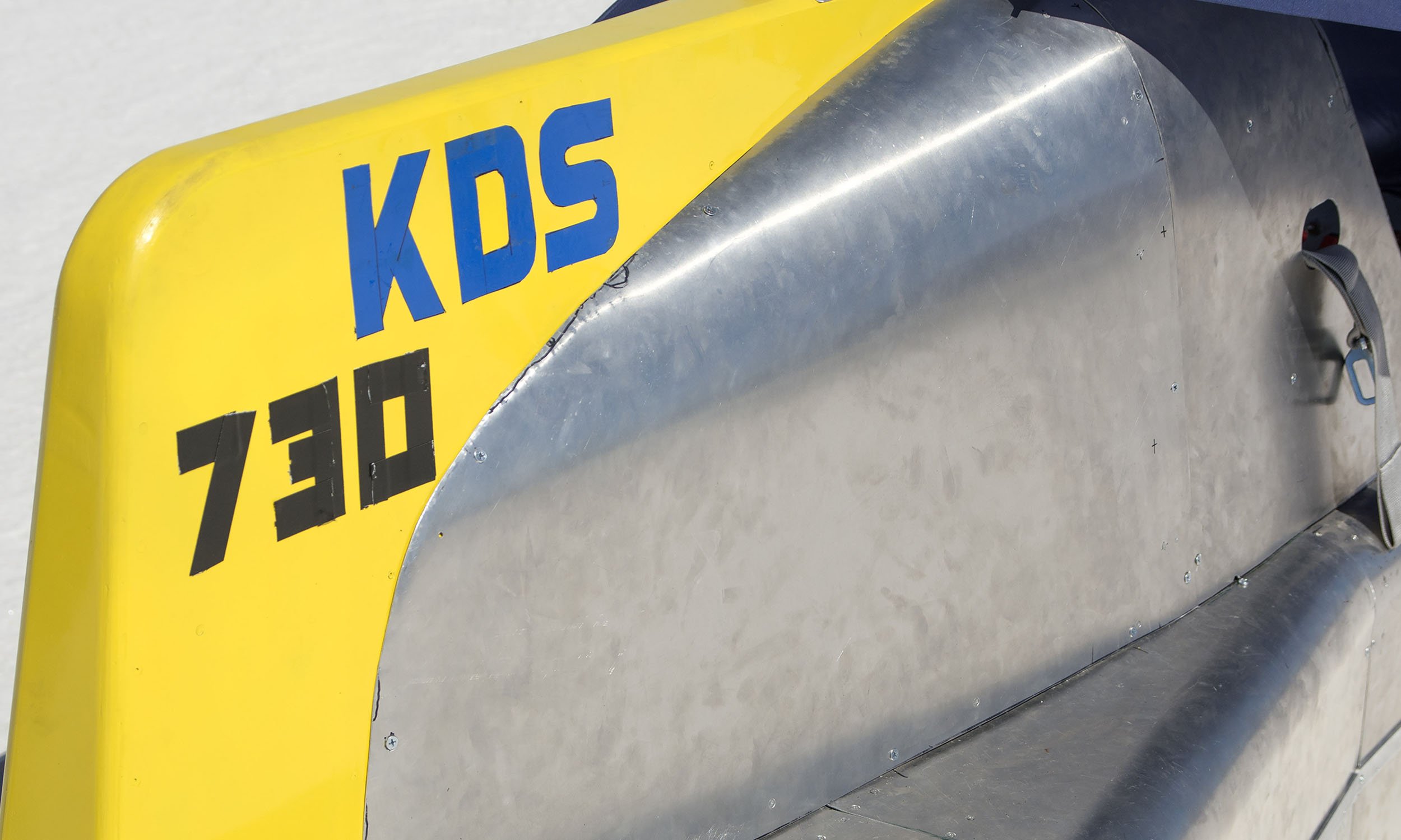 Close-up of a metallic object with a yellow and blue sticker that reads 'KUS' along with some other writing.