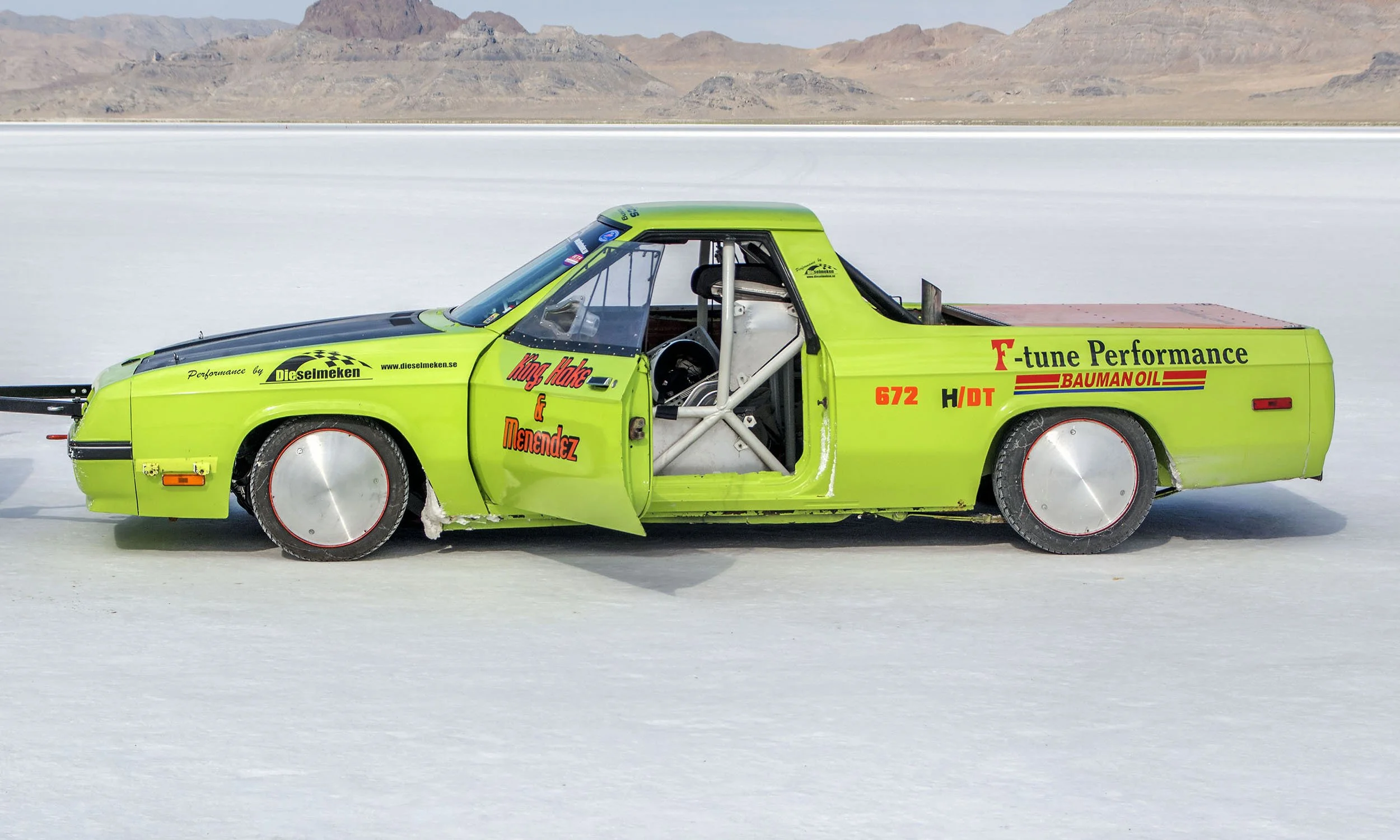 A bright lime green vintage race car on a salt flat, with the driver's side door open revealing a racing seat and roll cage, and surrounded by a vast flat salt surface with mountains in the background.