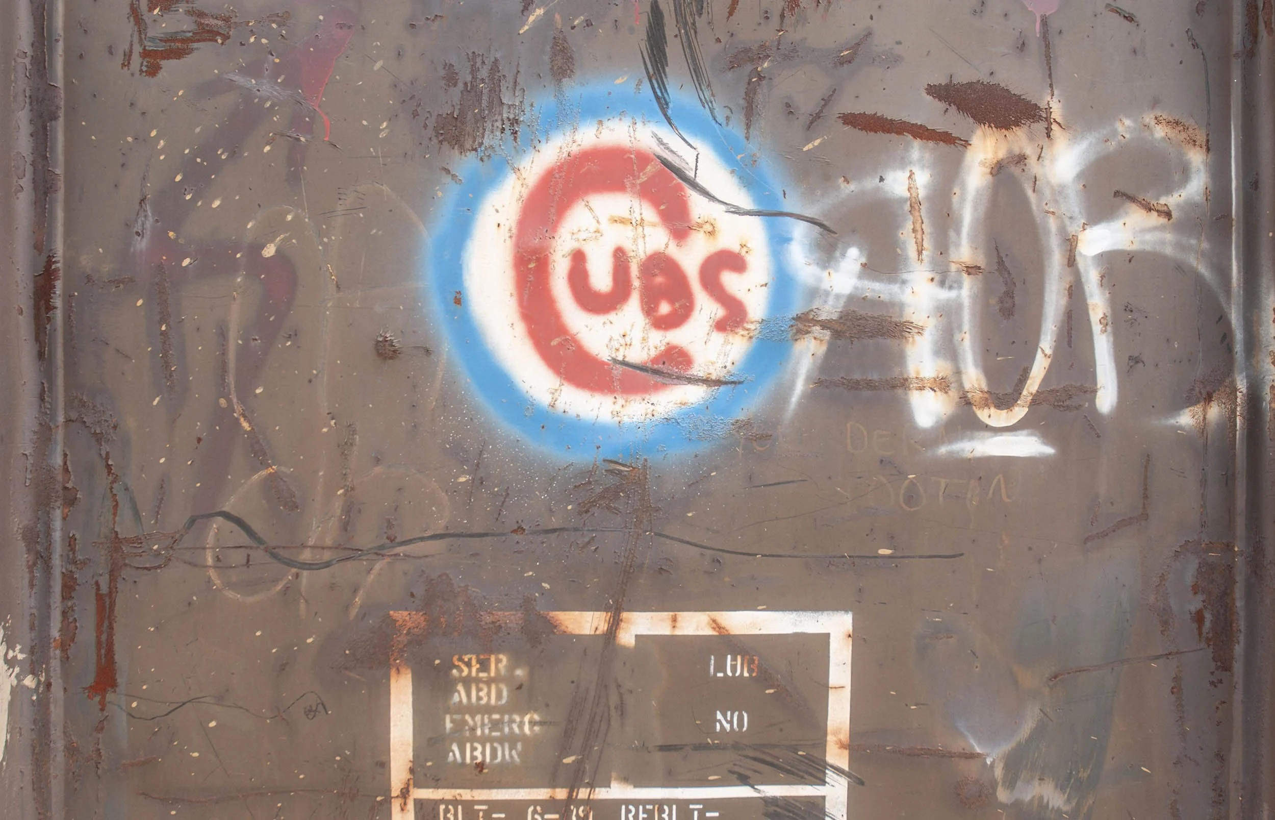 Rusty, scratched metal surface with an old, faded stencil that reads 'USE' in red letters inside a blue circle, and additional faded text below.