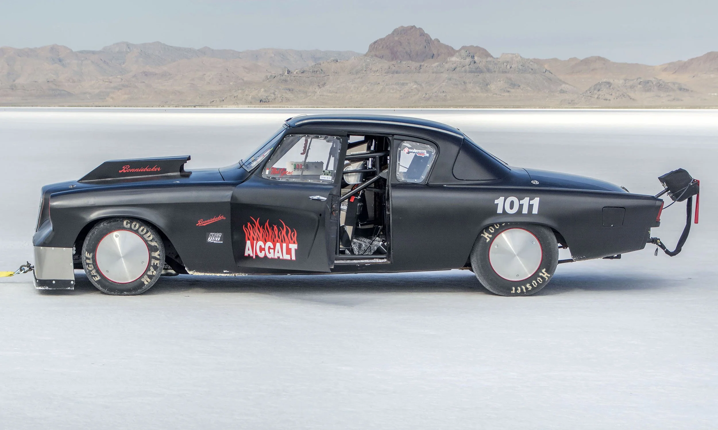Black drag racing car on a salt flat with mountains in the background, featuring the number 1011 and several sponsor stickers.
