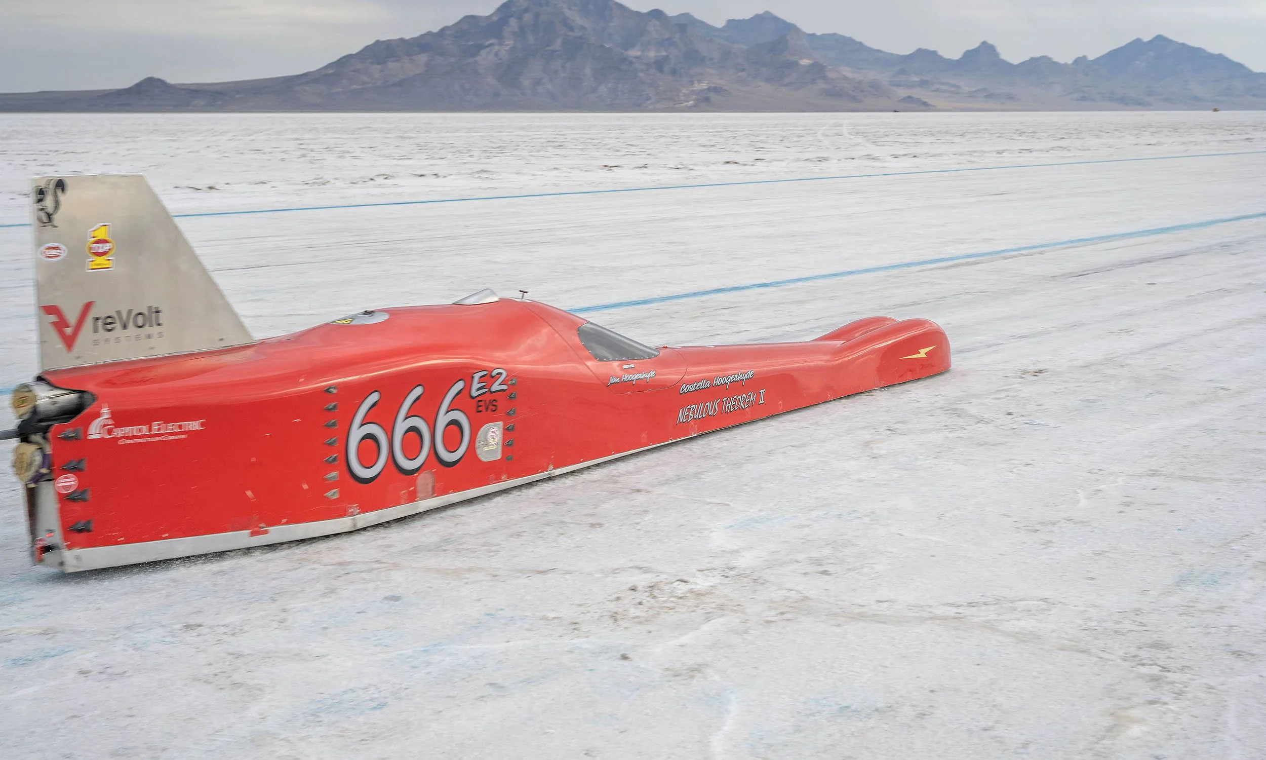A red race car with the number 666 on its side, driving on a salt flat with mountains in the background.