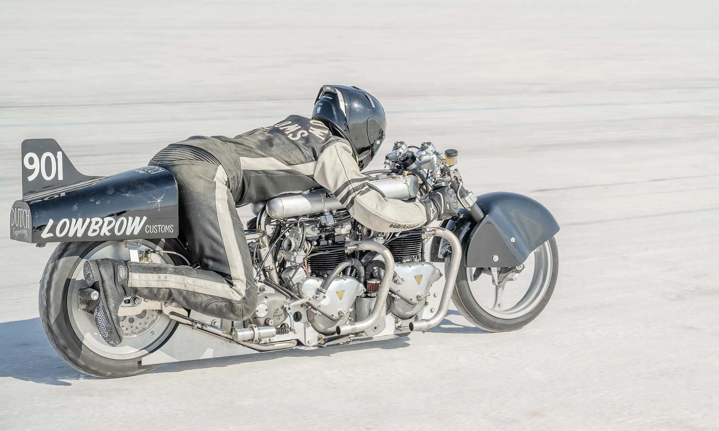 A person racing a motorcycle on a salt flat, twin-engine Triumph bike